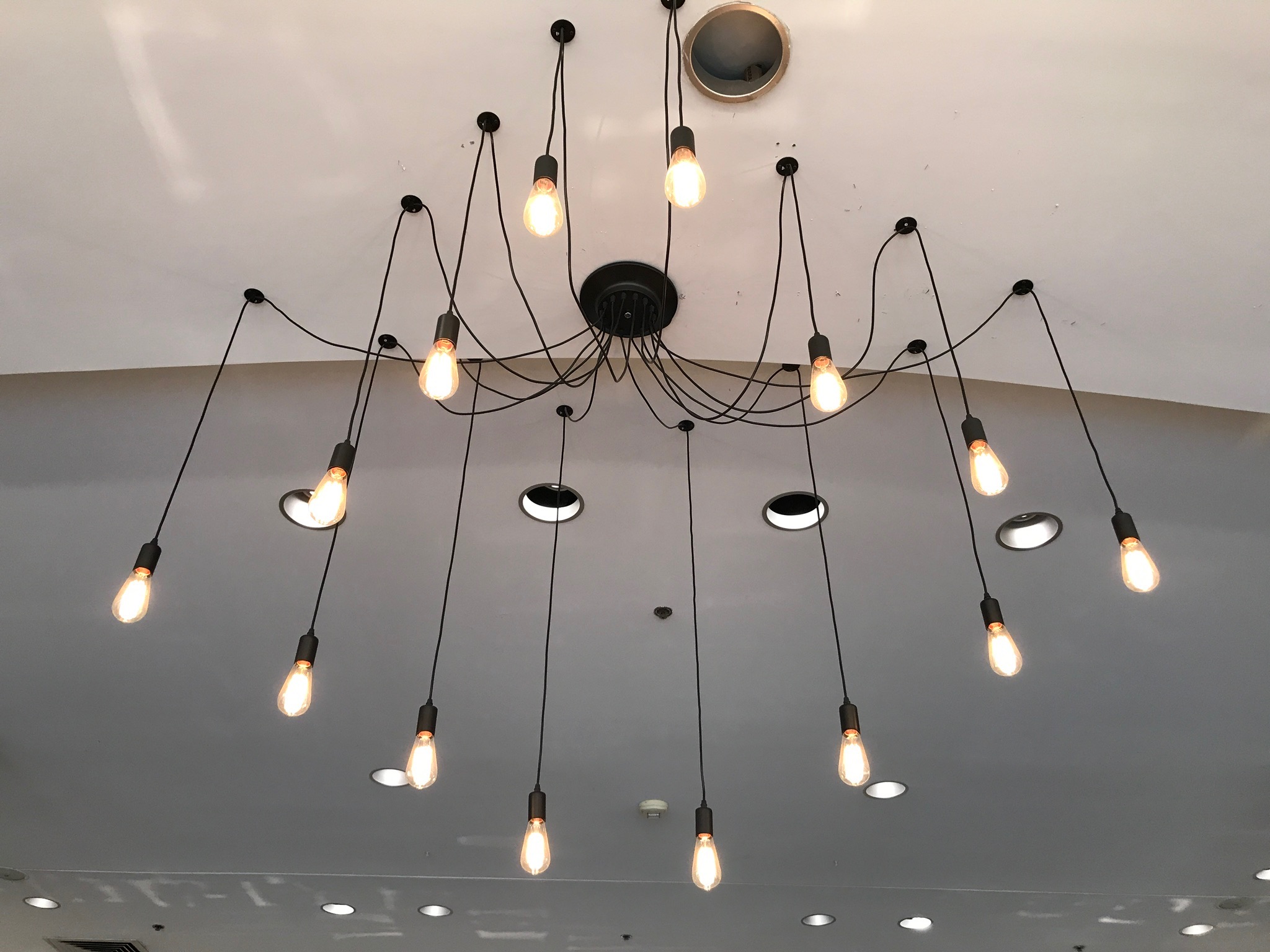 A modern chandelier with multiple exposed bulbs hanging from long black cords attached to a white ceiling.