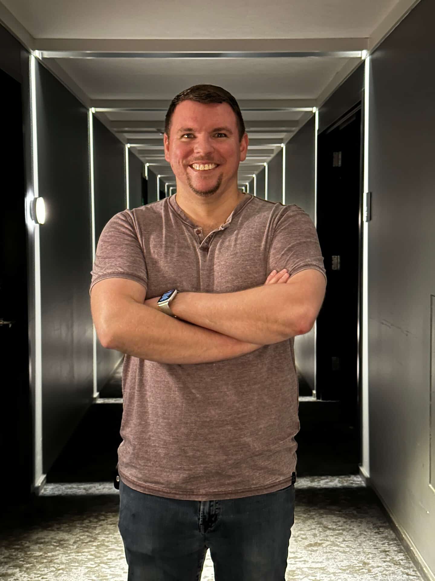 A man in a brown shirt and jeans stands with arms crossed in a well-lit Nashville hallway, accented by sleek geometric lighting.