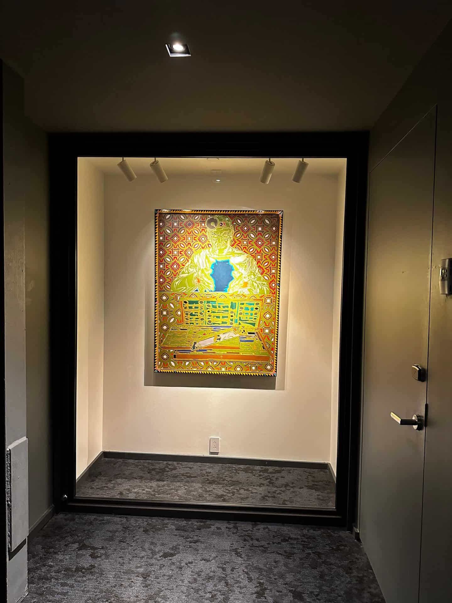 A brightly colored painting in a dimly lit alcove, depicting an abstract figure in a Nashville room with patterned walls, under a spotlight in a hallway.