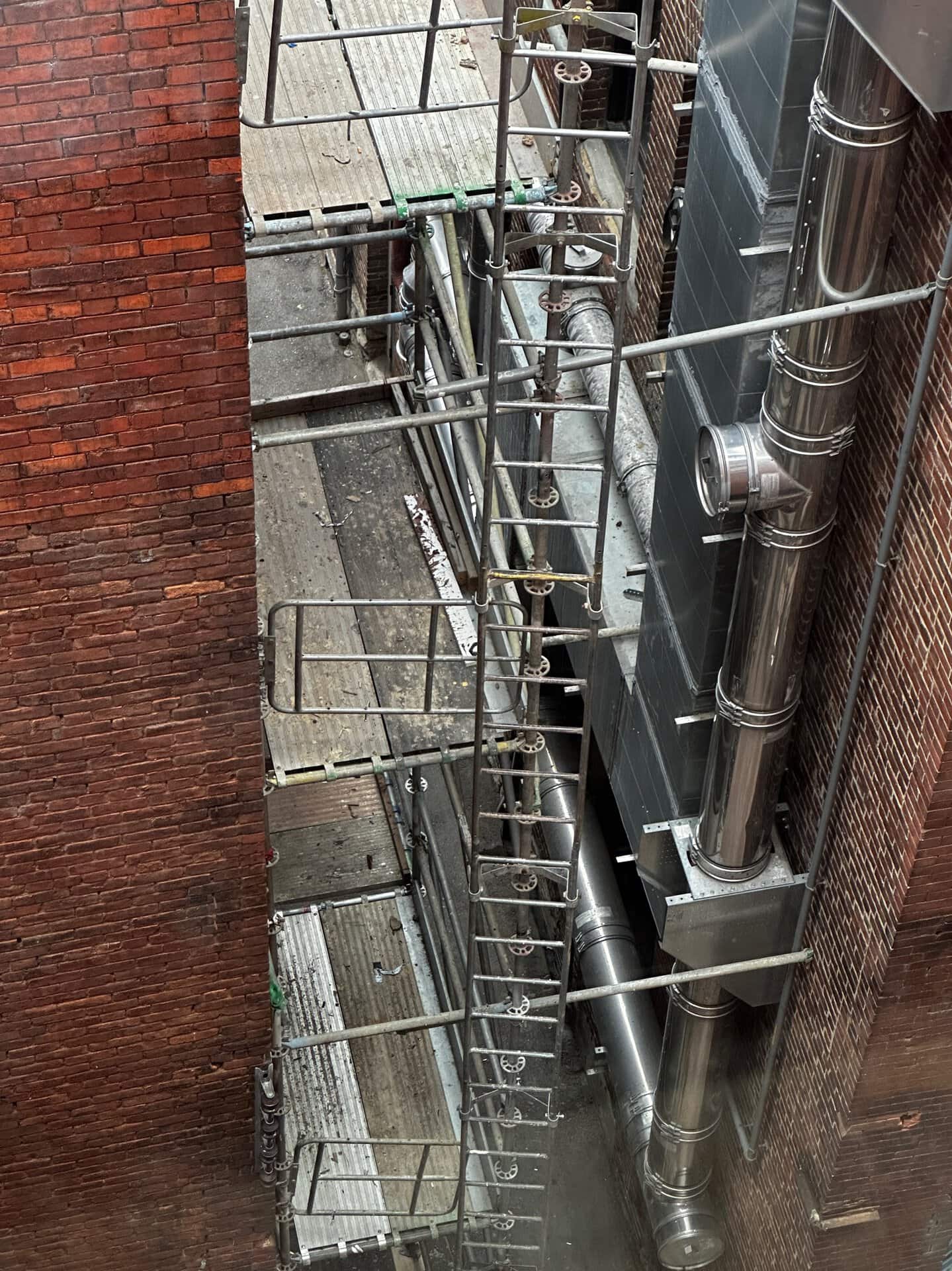 In a narrow Nashville alleyway between two brick buildings, metal scaffolding intertwines with ventilation pipes.
