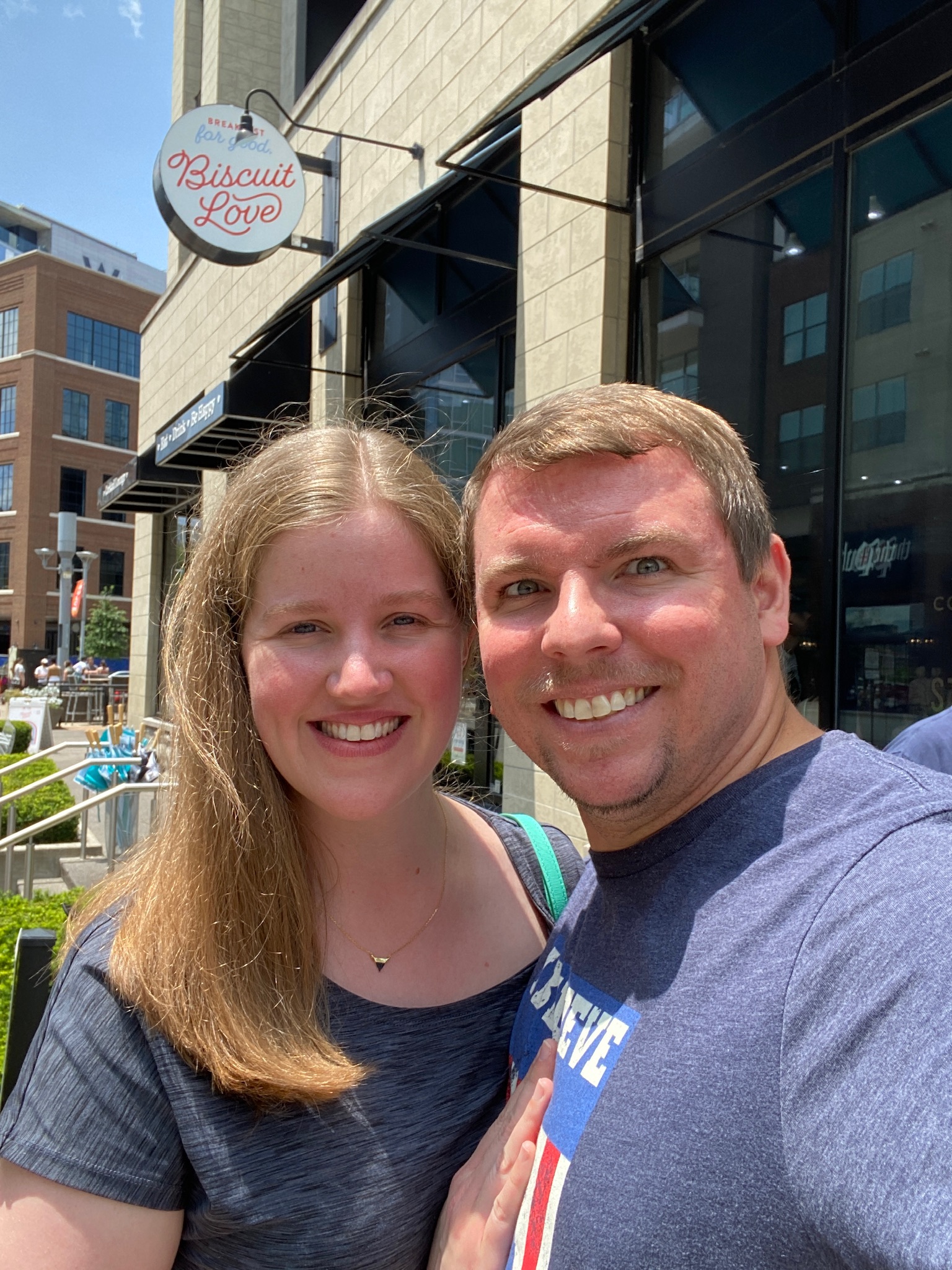 A smiling couple poses for a selfie outside Biscuit Love restaurant on a sunny day.