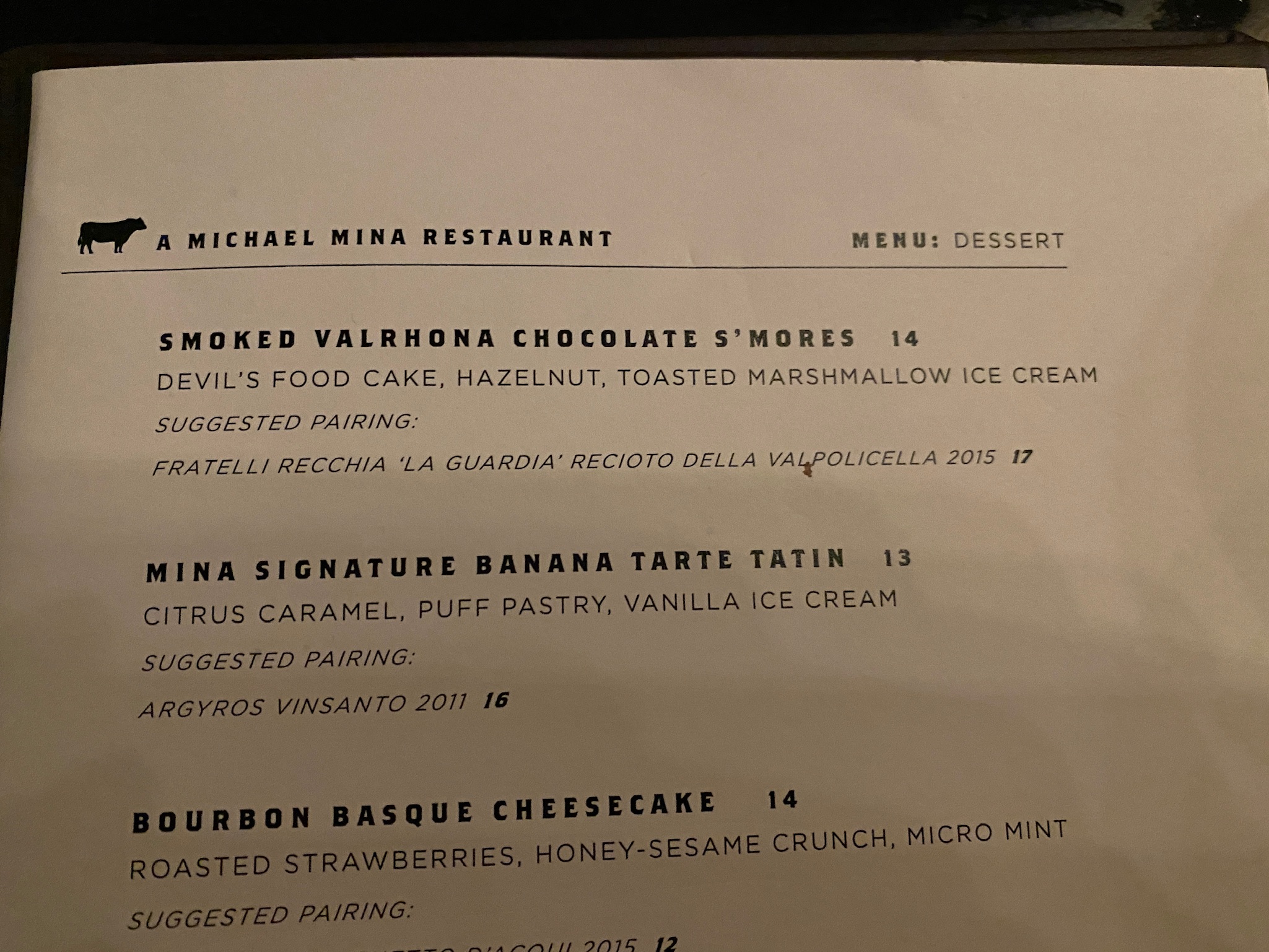 A dessert menu listing smoked Valrhona chocolate s’mores, banana tarte tatin, and bourbon basque cheesecake with suggested wine pairings.