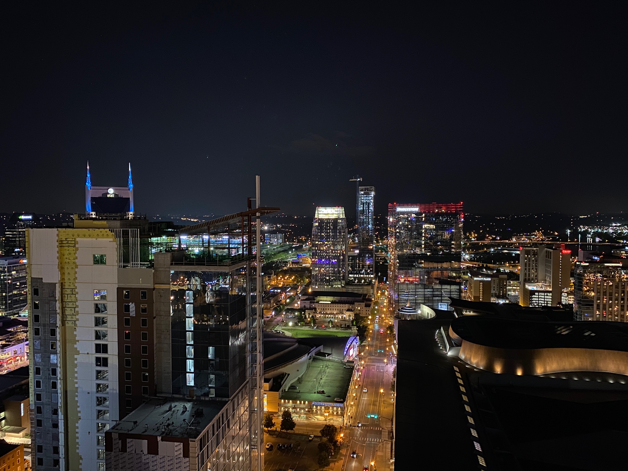 A nighttime cityscape with illuminated buildings, streets, and construction cranes, viewed from a high vantage point.