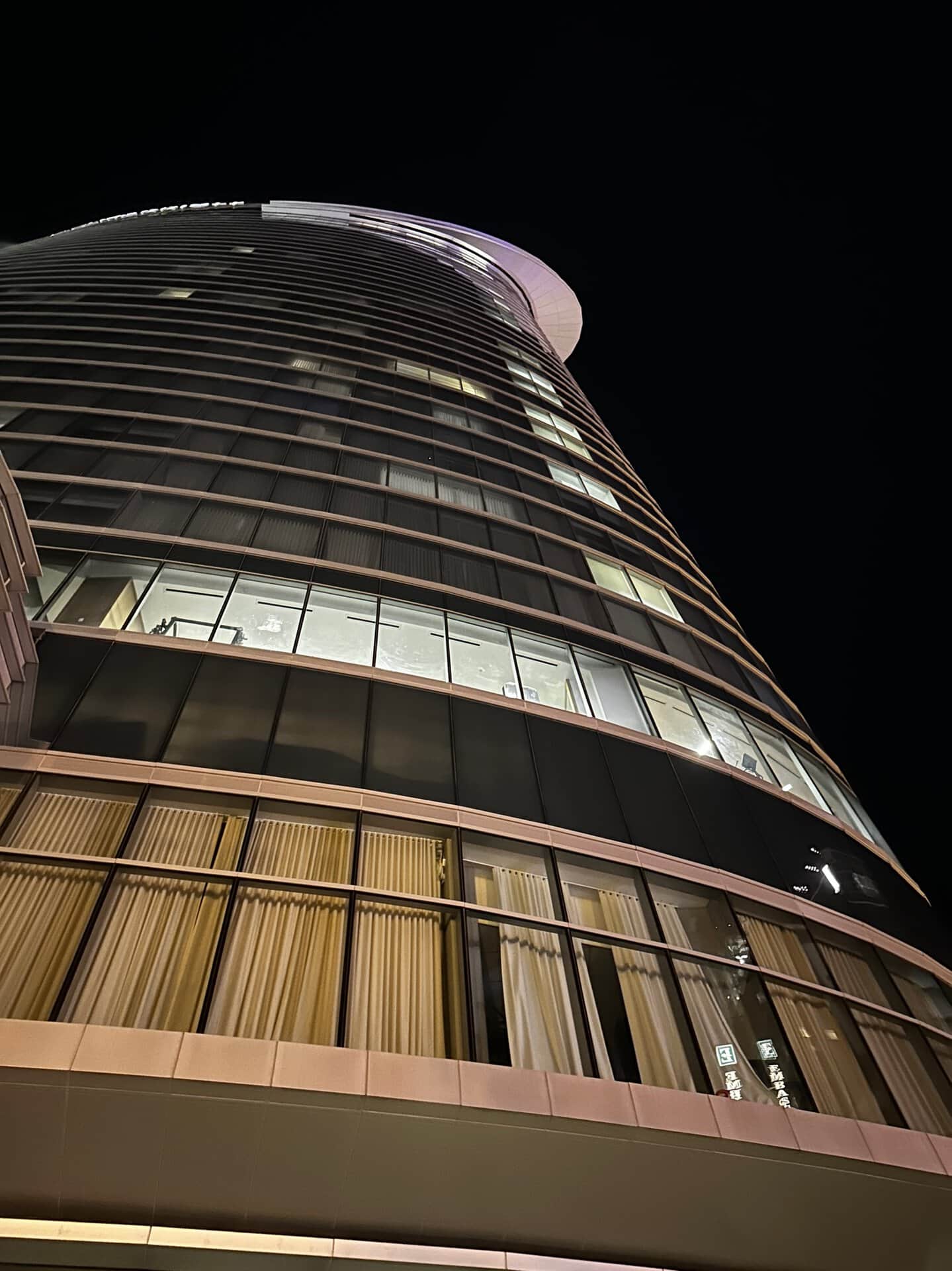 Night view of Nashville's modern, curved, glass-fronted skyscraper, shot from the ground looking up. The illuminated windows cast a warm glow against the dark sky.