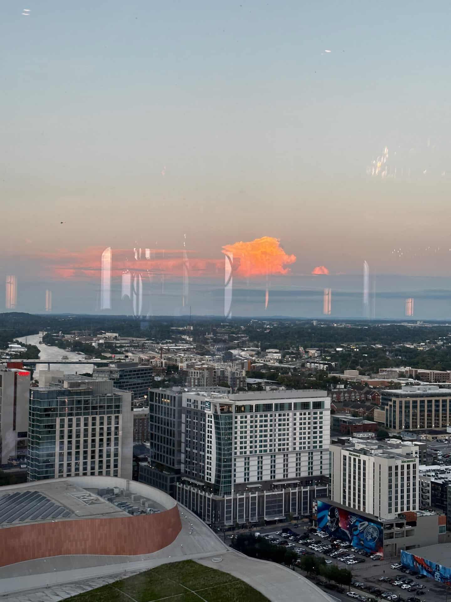 Experience the Nashville cityscape at sunset, where high-rise buildings and urban structures stand tall against a backdrop of orange clouds in the evening sky. The vibrant hues paint a stunning picture over this iconic skyline.