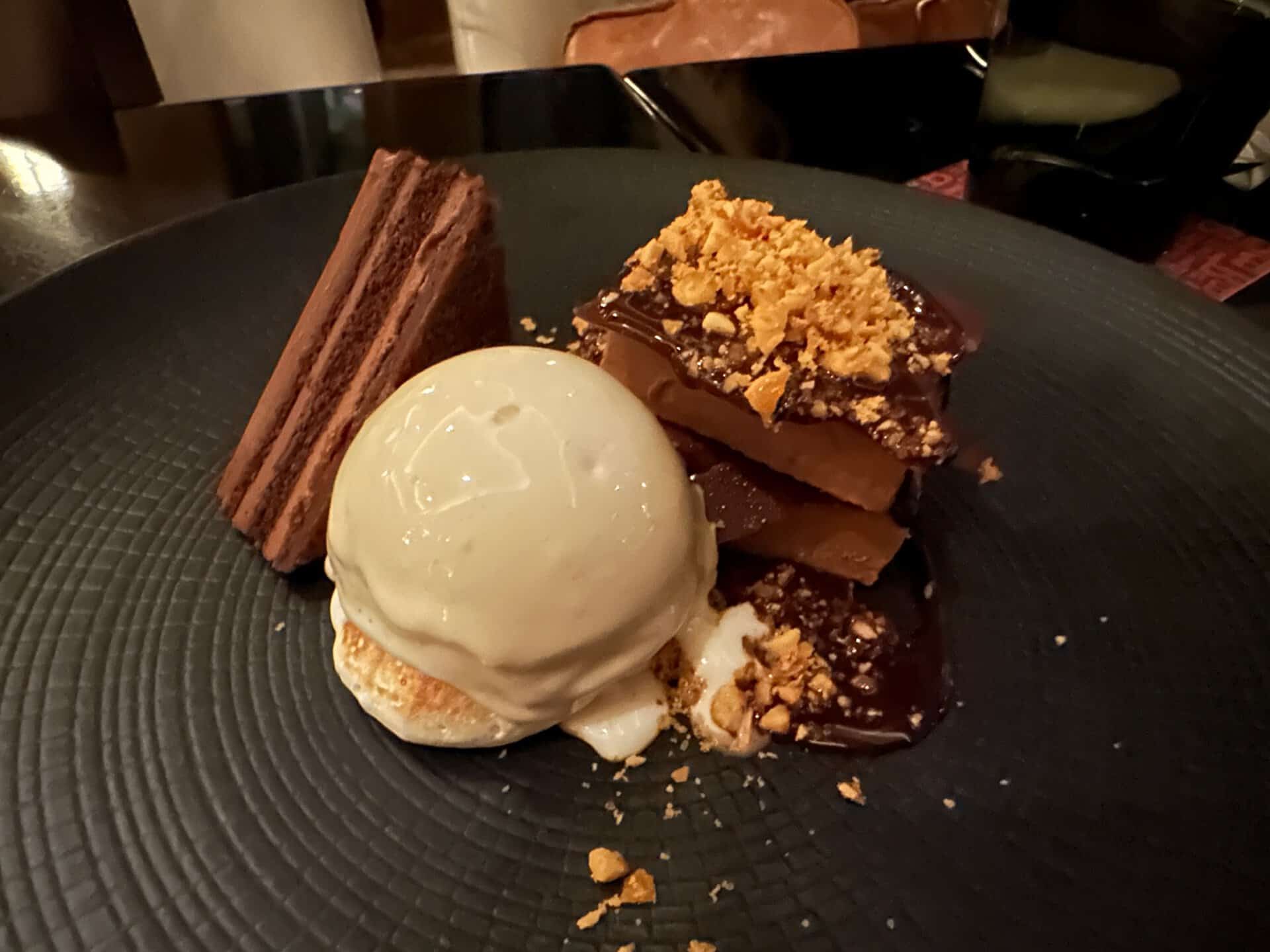 A Nashville-inspired dessert featuring a scoop of vanilla ice cream and layered chocolate cake topped with crumbles on a sleek black plate.
