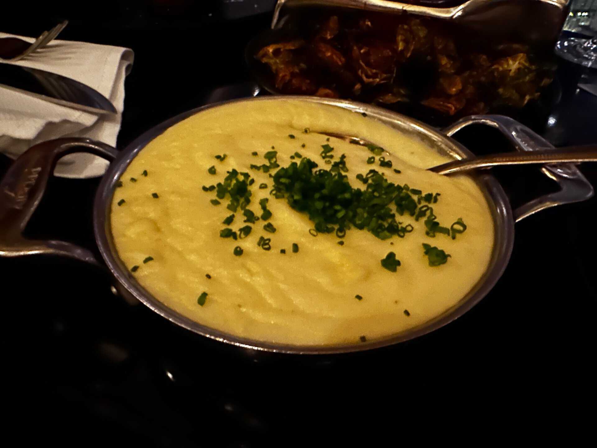 A pot of creamy mashed potatoes topped with chopped chives sits invitingly, reminiscent of a cozy Nashville kitchen. A spoon rests in the pot, and a plate of food is partially visible in the background.