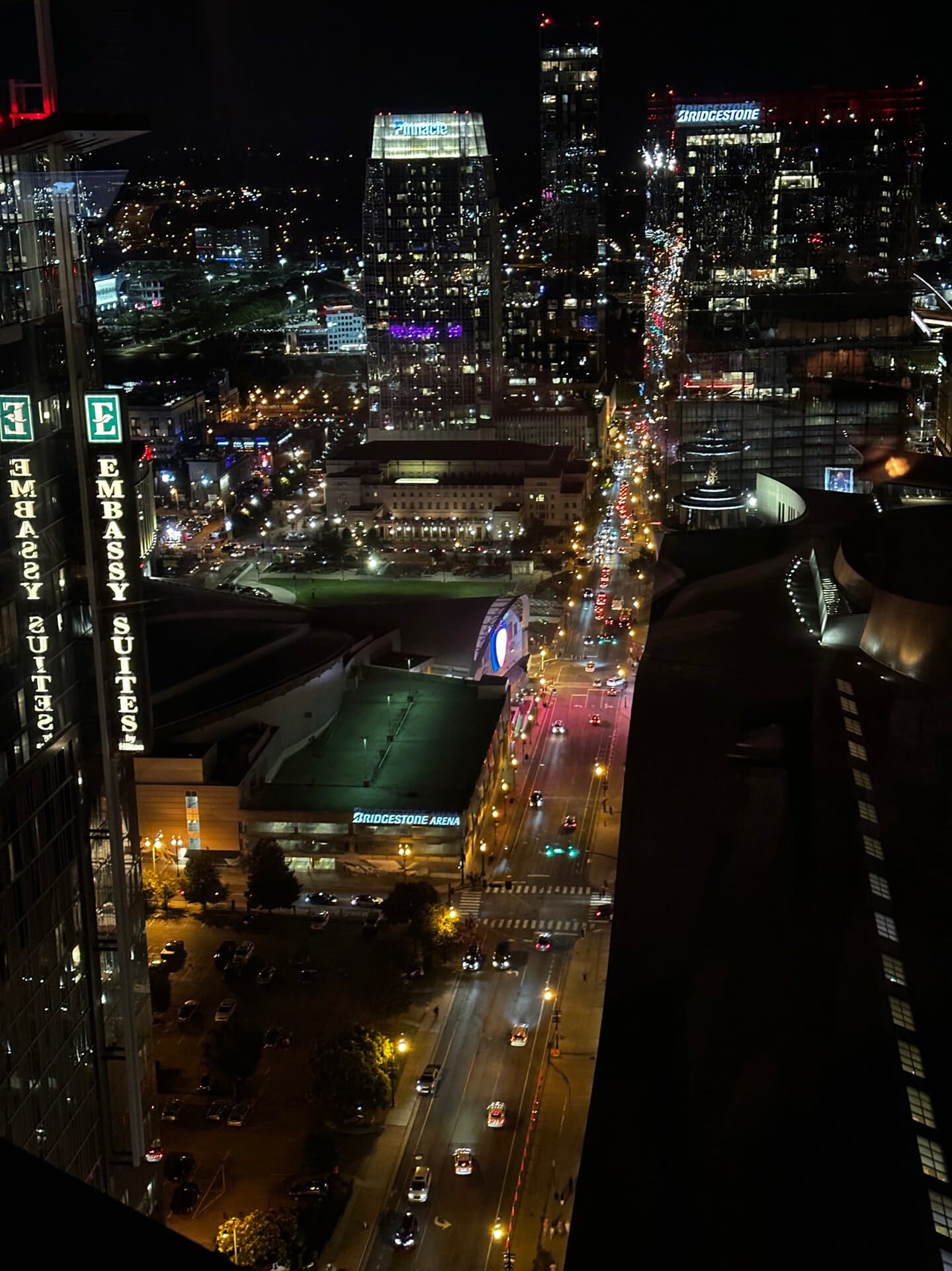 Nighttime aerial view of a vibrant Nashville cityscape with illuminated buildings, streets filled with car lights, and the lively signage of hotels painting a picturesque scene.