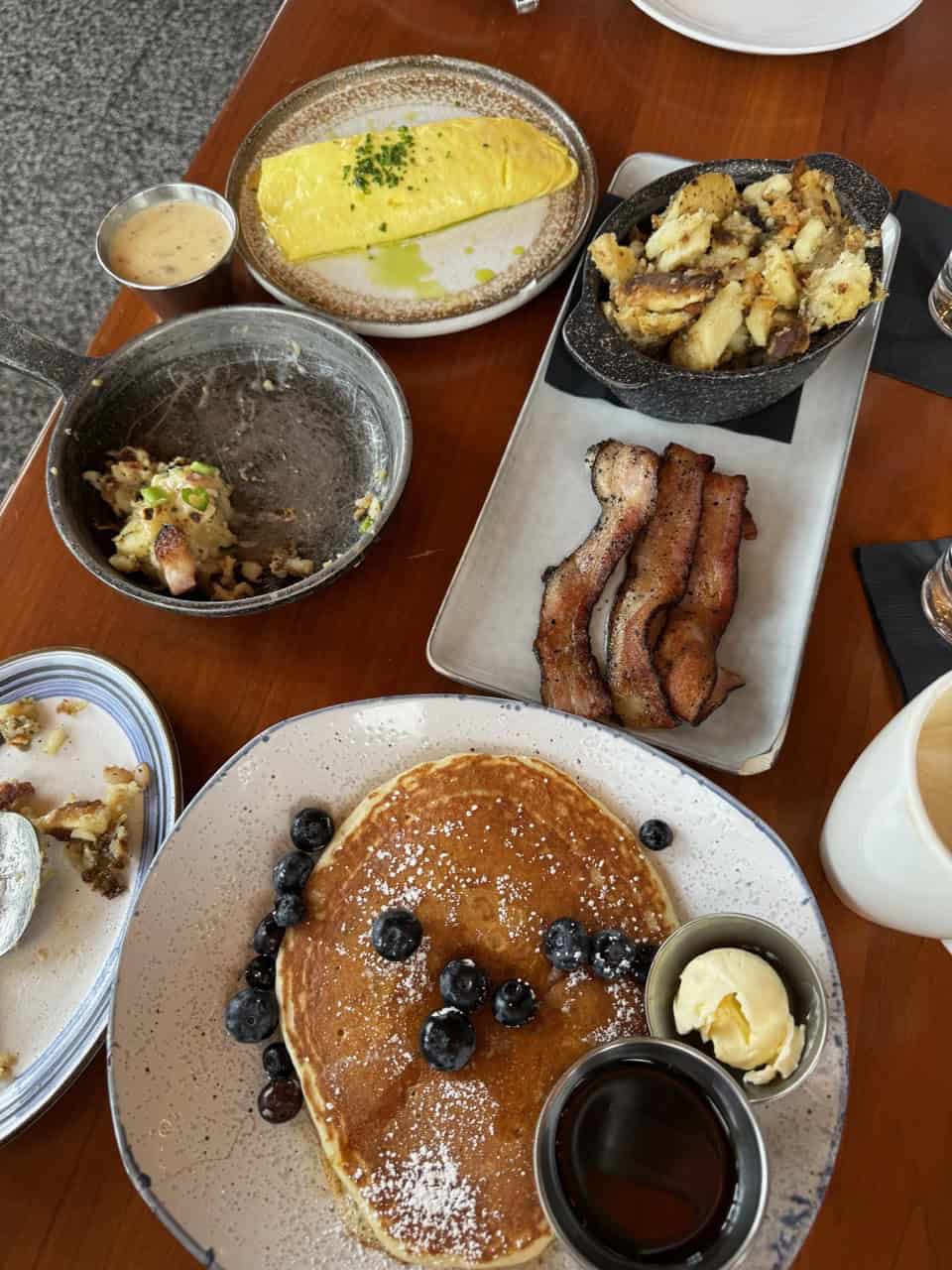 A Nashville brunch table boasts fluffy pancakes with blueberries, crispy bacon strips, scrambled eggs sprinkled with herbs, golden roasted potatoes, and a steaming cup of coffee.
