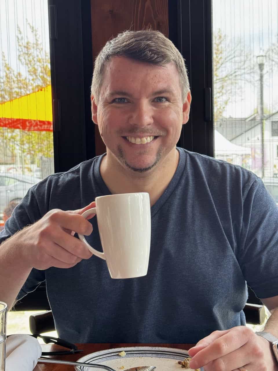 Man smiling and holding a white mug while sitting at a table in a Nashville restaurant.