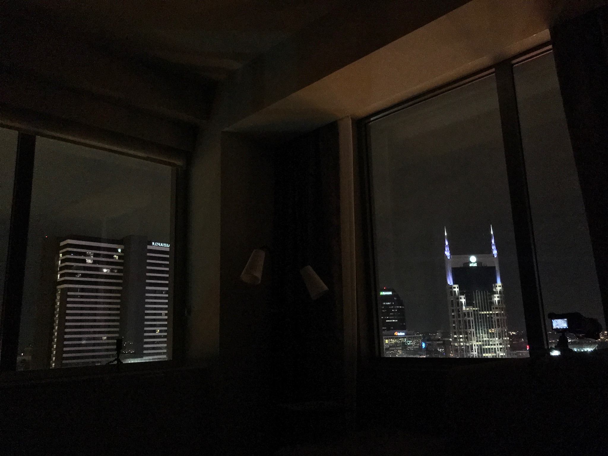 Nighttime cityscape view from a window, showing illuminated office buildings and a tower with two lit spires against a dark sky.