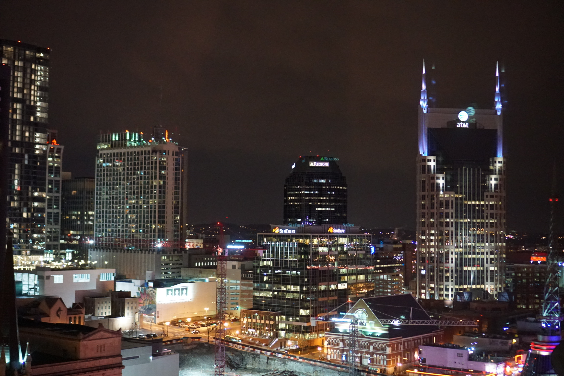 Nighttime cityscape of downtown Nashville with illuminated office buildings, including the AT&T building, and streets lit by streetlights.