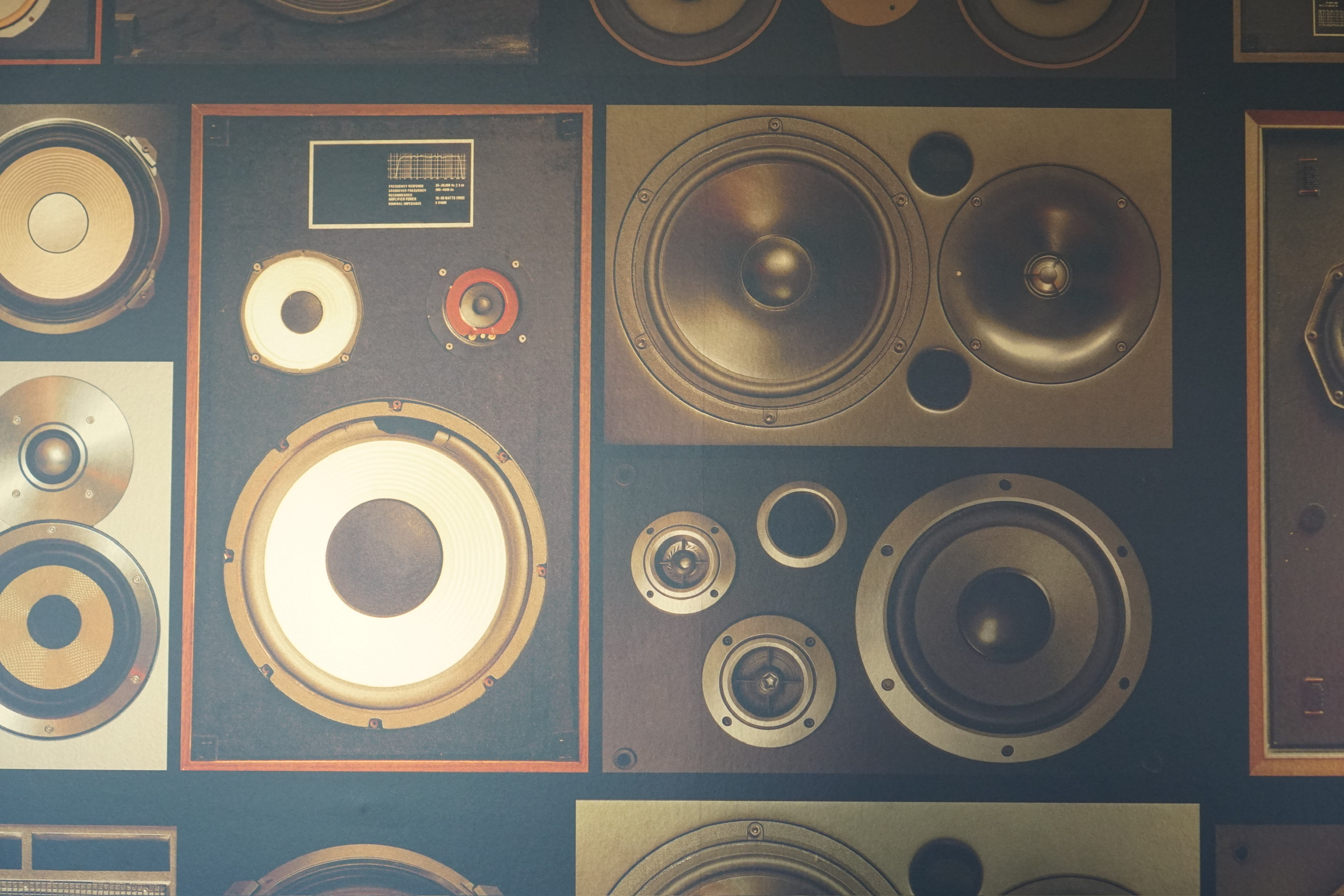 A close-up view of a wall decorated with various vintage speaker fronts and audio equipment arranged in a grid pattern.