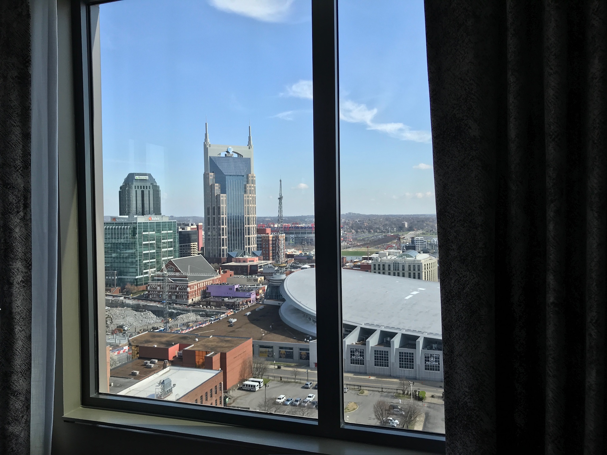 View through a window showing downtown Nashville, including the AT&T Building, city buildings, and part of the Bridgestone Arena under a clear blue sky.