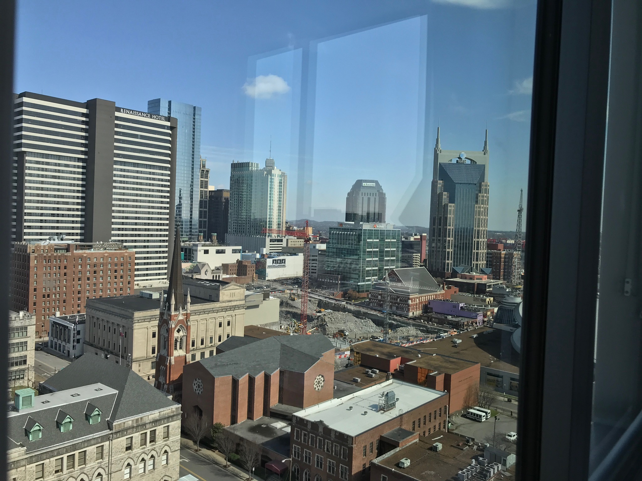 View of a cityscape with modern and historic buildings, seen through a window with reflections, under a clear blue sky.