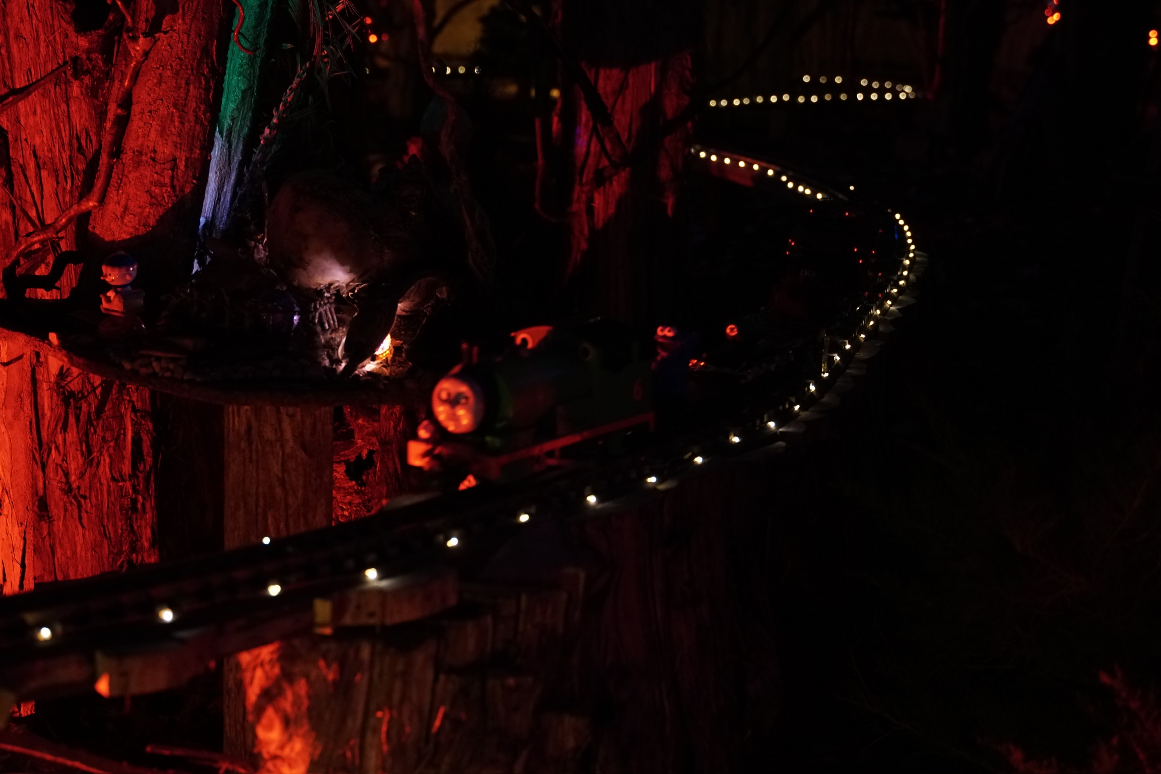 A toy train with a face moves along a track lined with small lights in a dimly lit, Nashville-inspired, forest-themed setting.