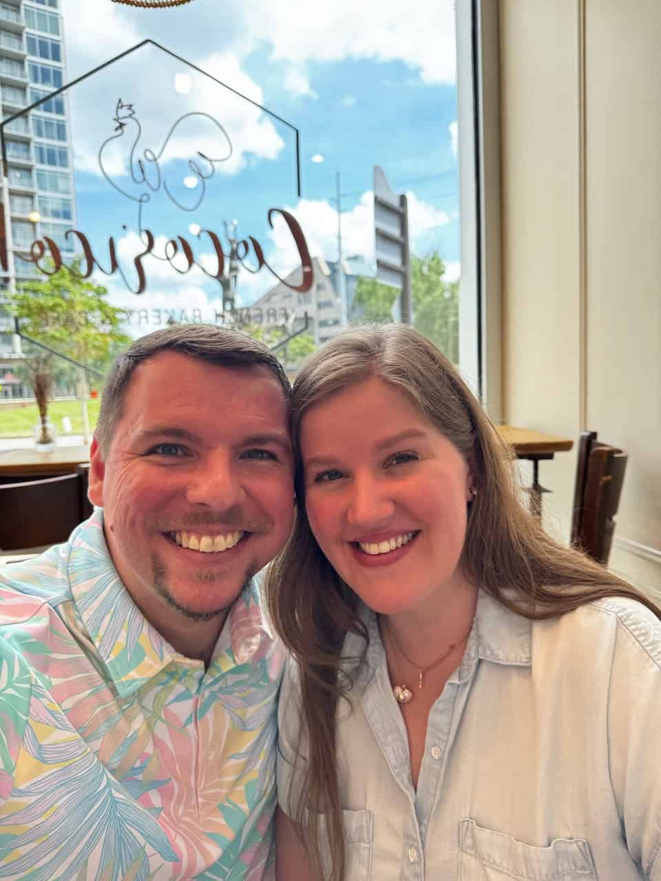 A man and woman smiling, sitting inside a Nashville cafe with the city's vibrant skyline visible through the window behind them.