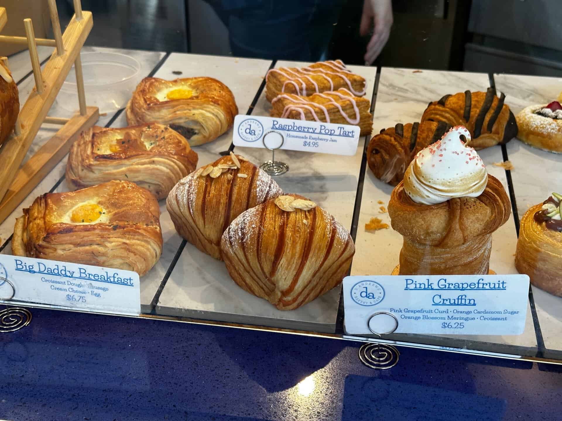 A delightful Nashville twist on pastries features a croissant with egg, a raspberry pop tart, and a pink grapefruit cruffin, each elegantly priced.