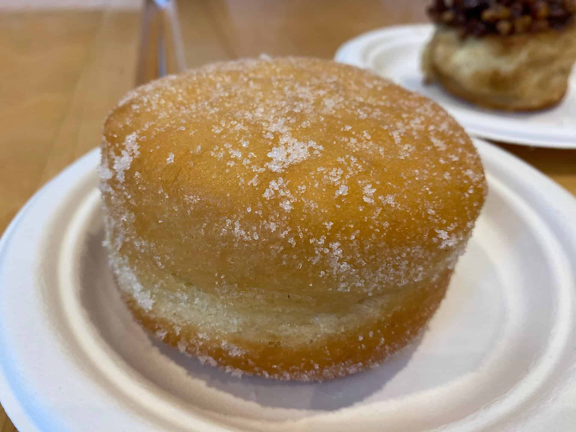 A sugar-coated doughnut, reminiscent of a Nashville treat, sits on a white paper plate with another doughnut partially visible in the background.