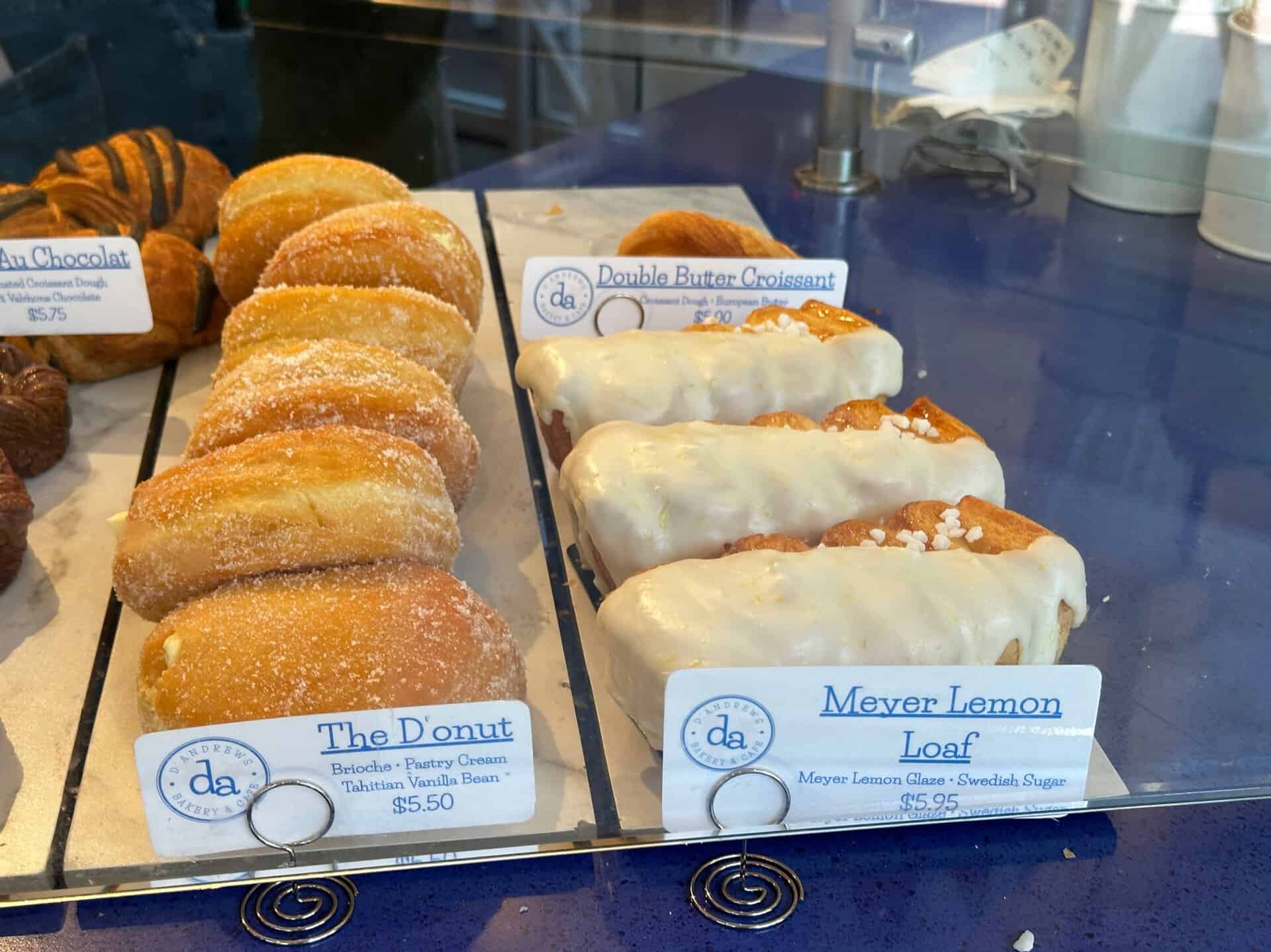 Nashville bakery display featuring an array of pastries: sugared donuts, double butter croissants, and Meyer lemon loaves with glaze. Each treat is elegantly labeled with a price tag, inviting you to savor a taste of Southern charm.