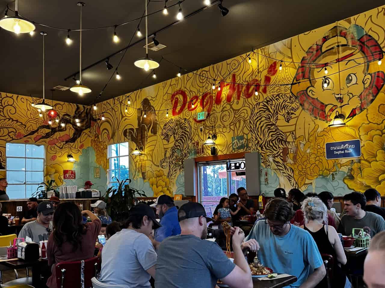 People dining in a brightly lit Nashville restaurant, with a large mural featuring vibrant colors and intricate designs on the wall.