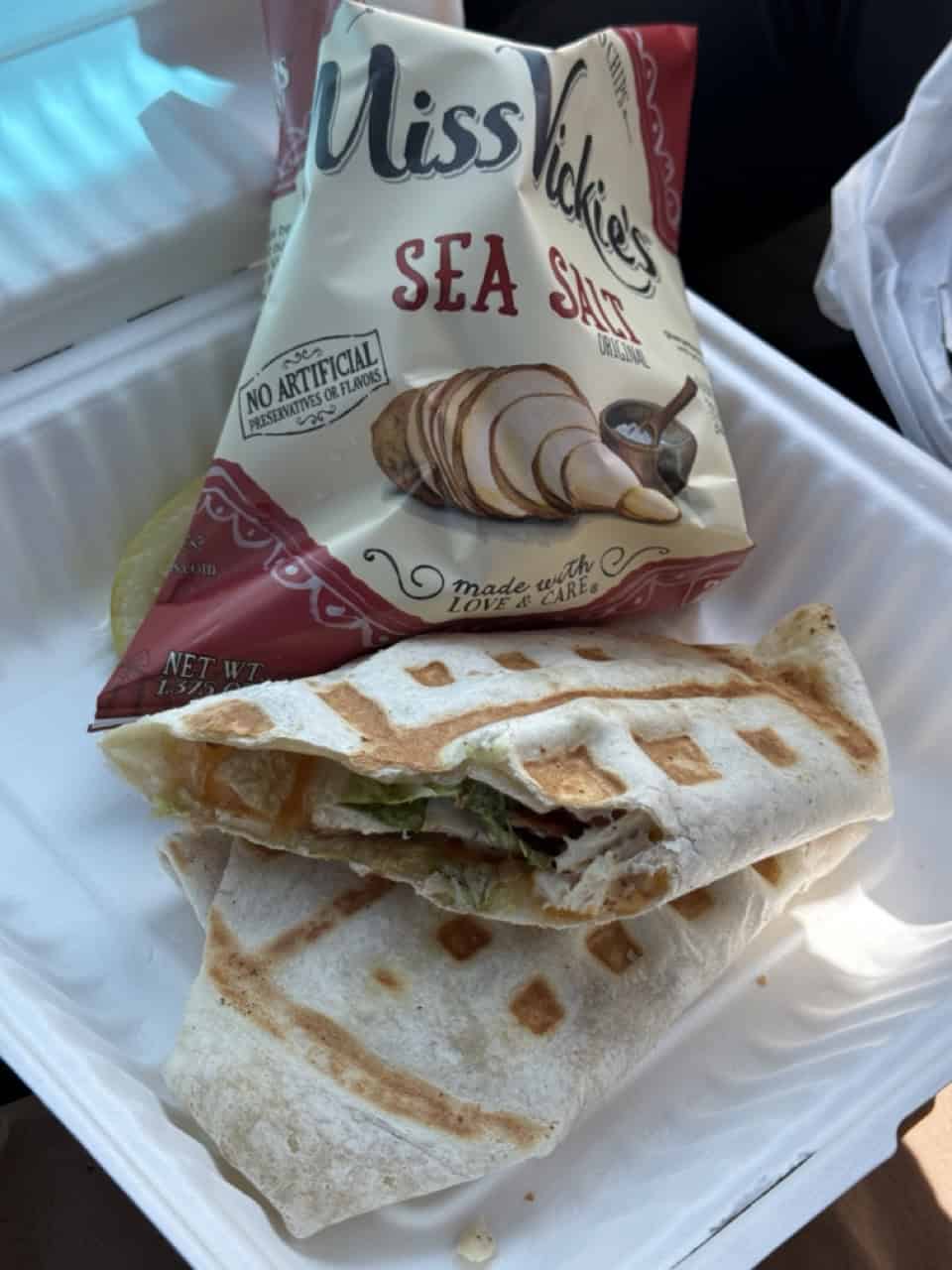 A halved wrap sandwich nestles in its takeout container, topped with a bag of Miss Vickie's Sea Salt chips. This convenient meal feels right at home in the lively streets of Nashville, where every bite tells its own story.