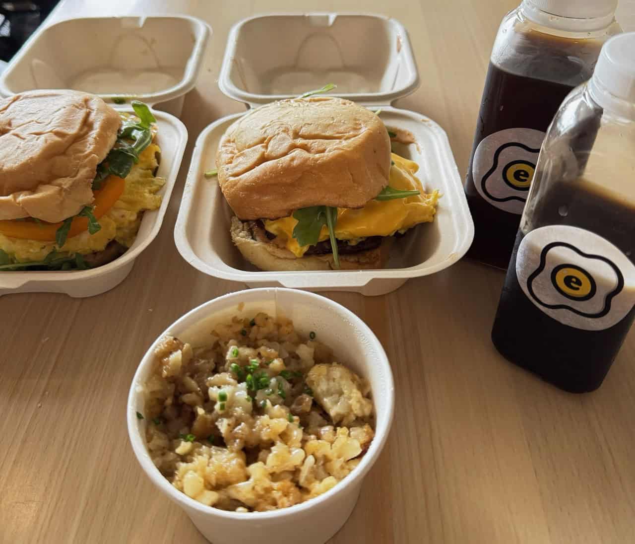 Two Nashville-style breakfast sandwiches, a cup of rice, and two bottles of coffee rest elegantly on the wooden table.