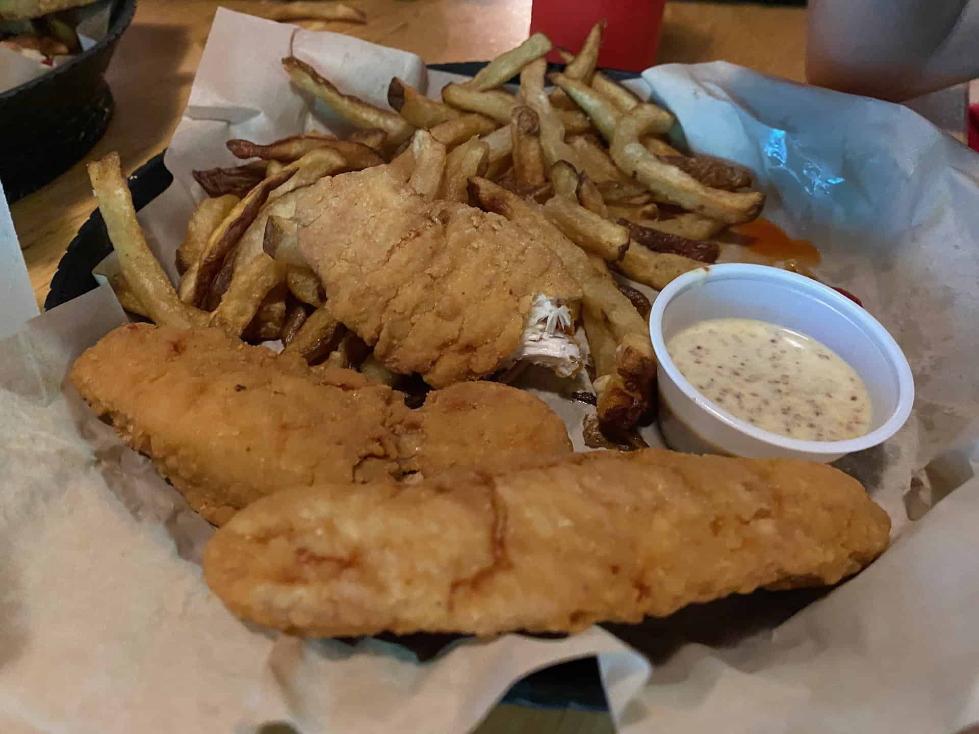 Fried fish and French fries on parchment paper with a side of mustard sauce in a small cup.