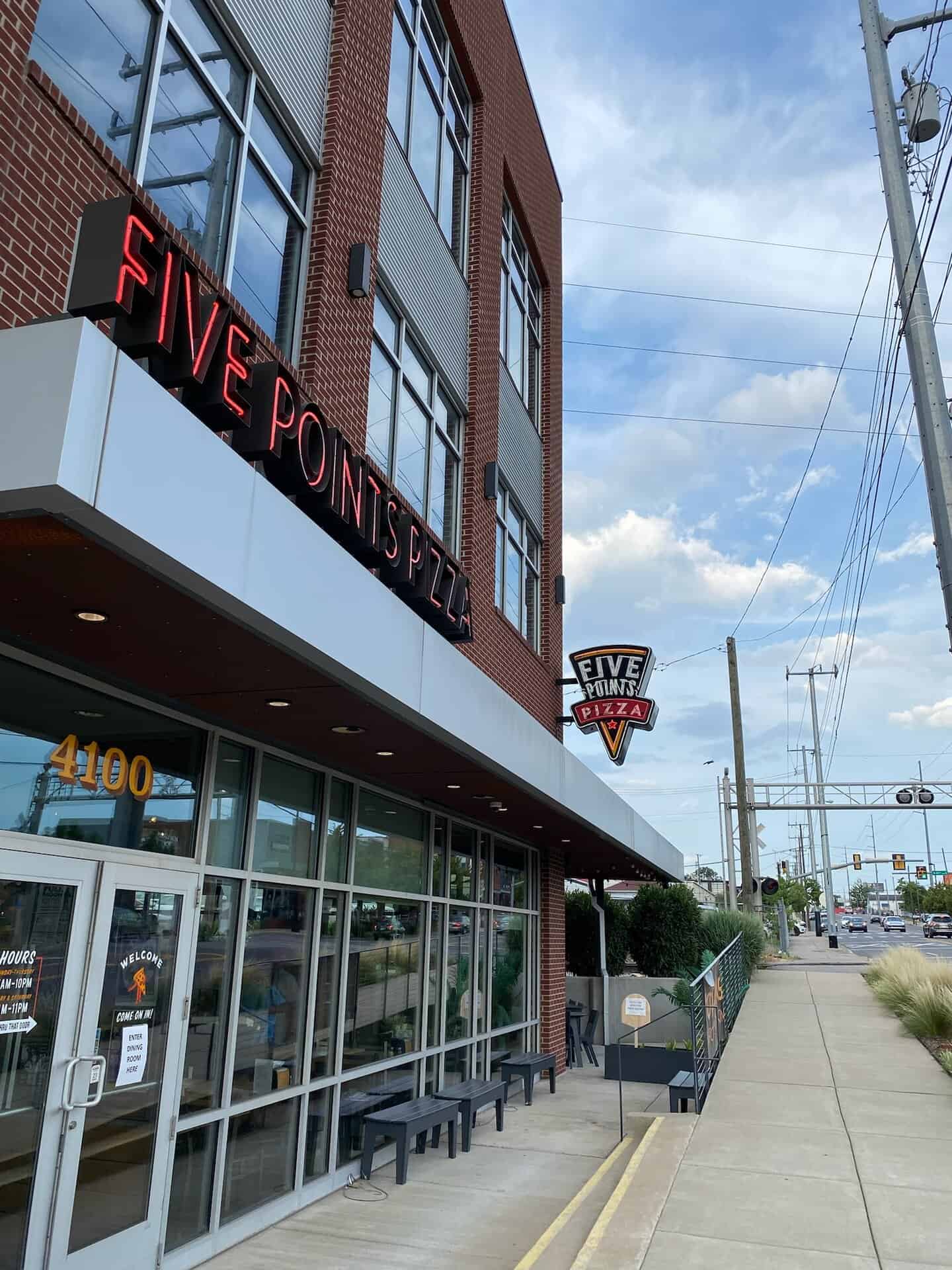 Street view of Five Points Pizza, a brick building with red signage, located next to a sidewalk under a partly cloudy sky.