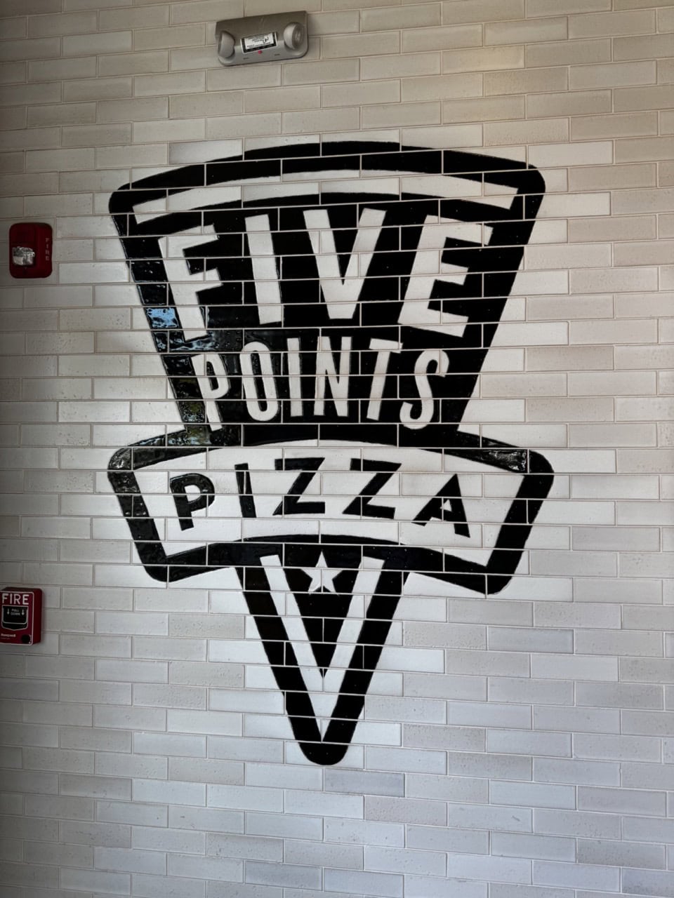 The black and white "Five Points Pizza" logo stands out on the tiled wall, capturing the spirit of Nashville, with a nearby fire alarm adding a touch of practicality.