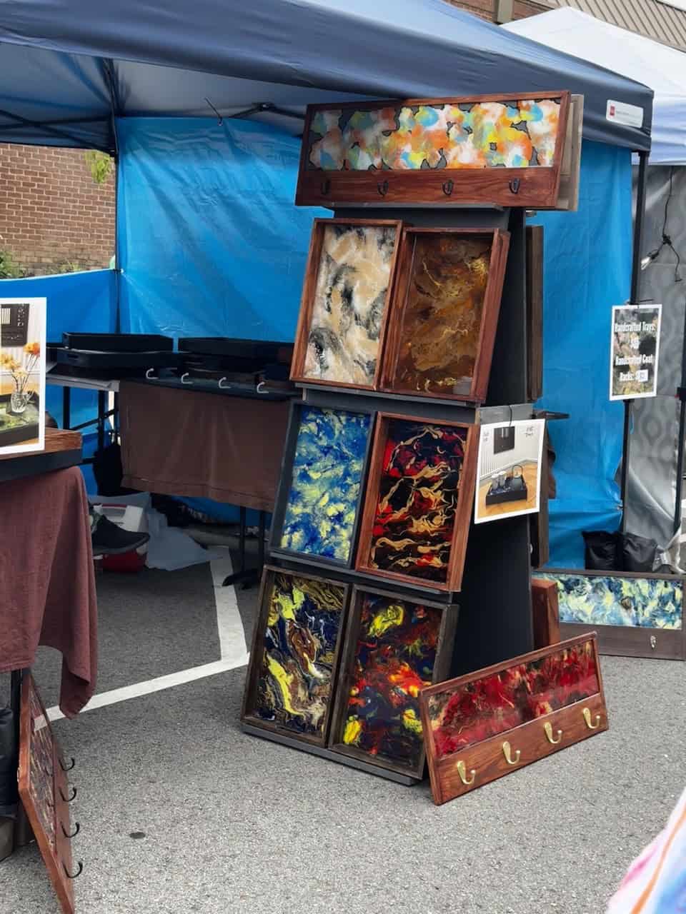 A vibrant outdoor market stall in Nashville showcases colorful abstract art pieces and sleek coat racks under a striking blue canopy.