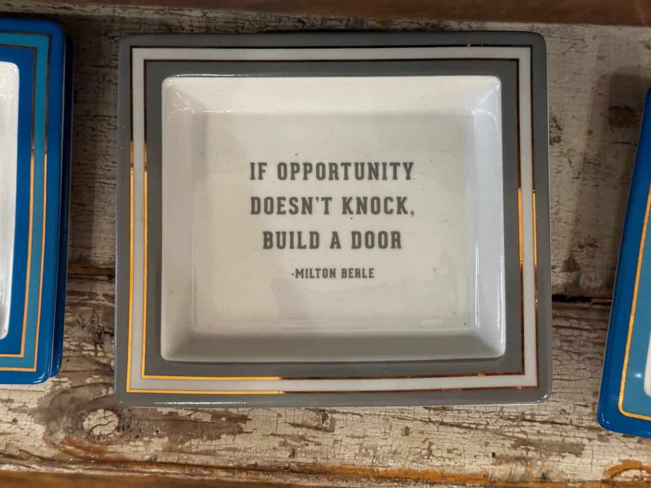 A square dish featuring the inspiring quote "If opportunity doesn't knock, build a door - Milton Berle" at its center, perfect for any Nashville-themed decor.
