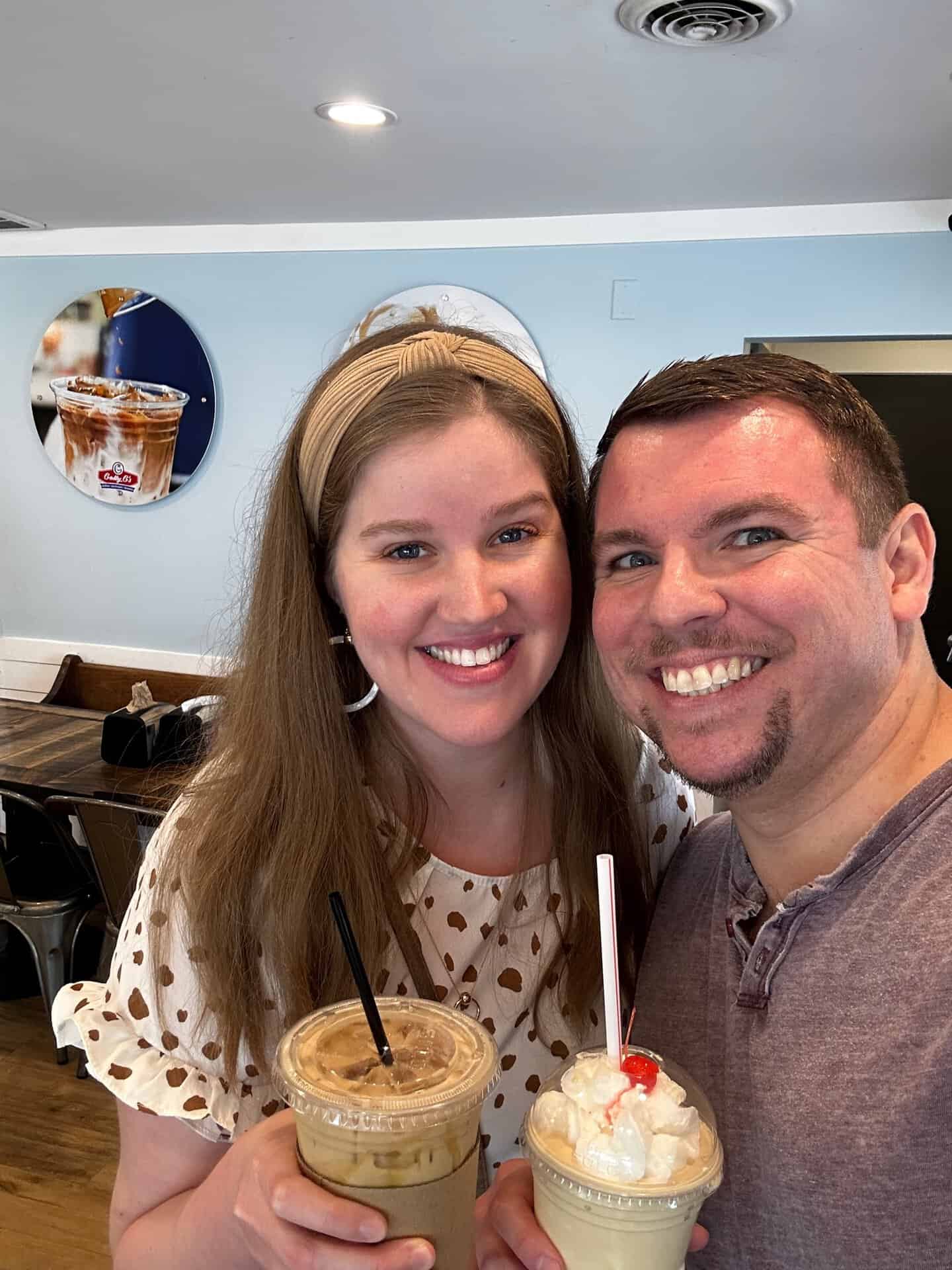 Two people smiling and holding iced drinks topped with whipped cream and cherries in a charming Nashville cafe.