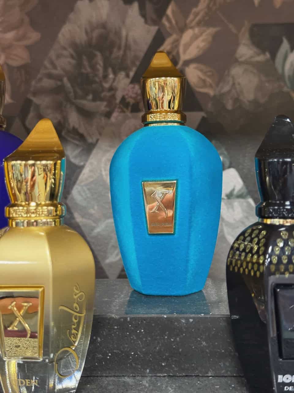 A collection of luxury perfume bottles with gold and blue caps, reminiscent of Nashville's vibrant spirit, features a central blue bottle with a gold emblem on a display shelf.
