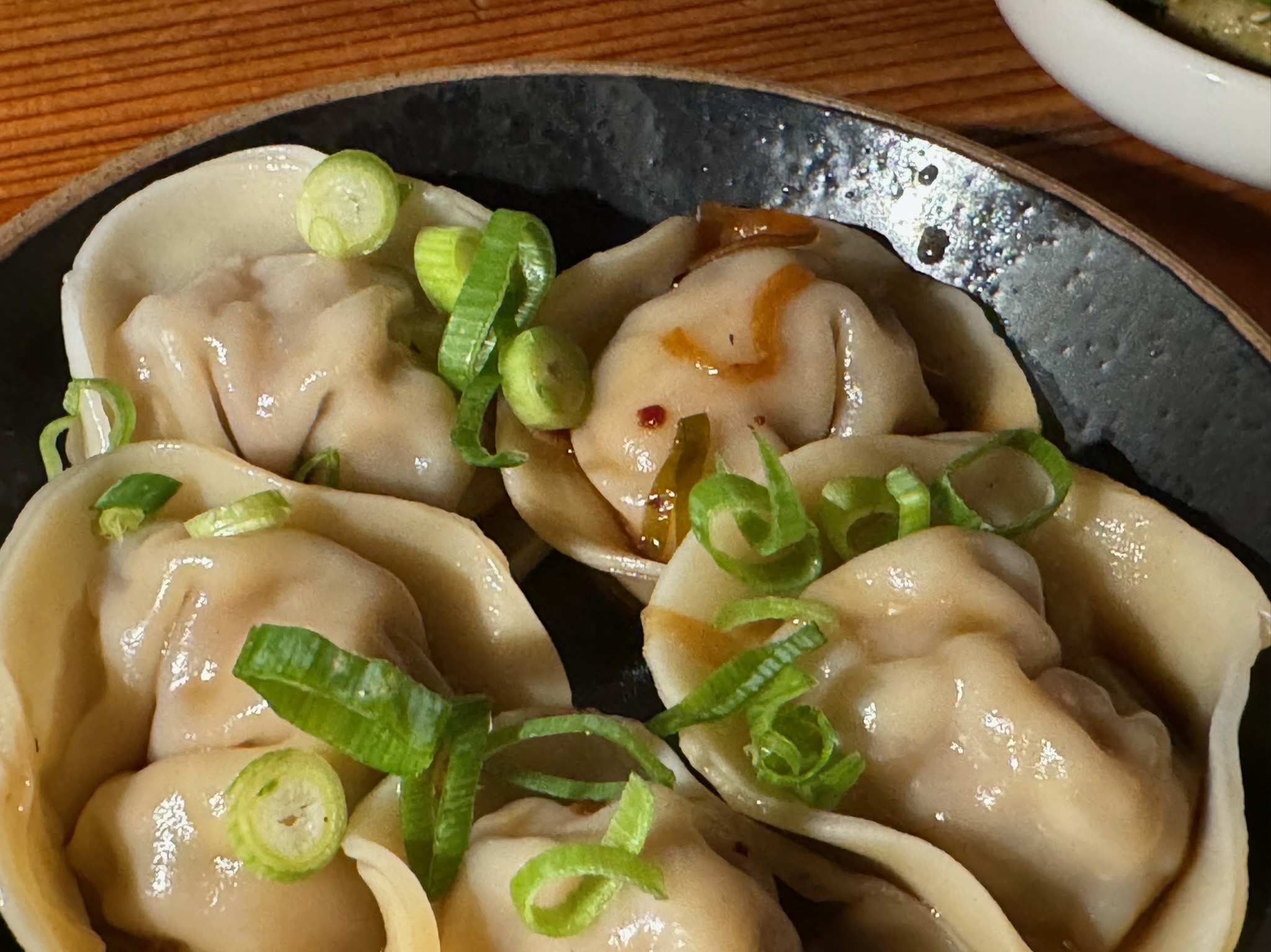 A close-up of five steamed dumplings topped with sliced green onions on a black plate.