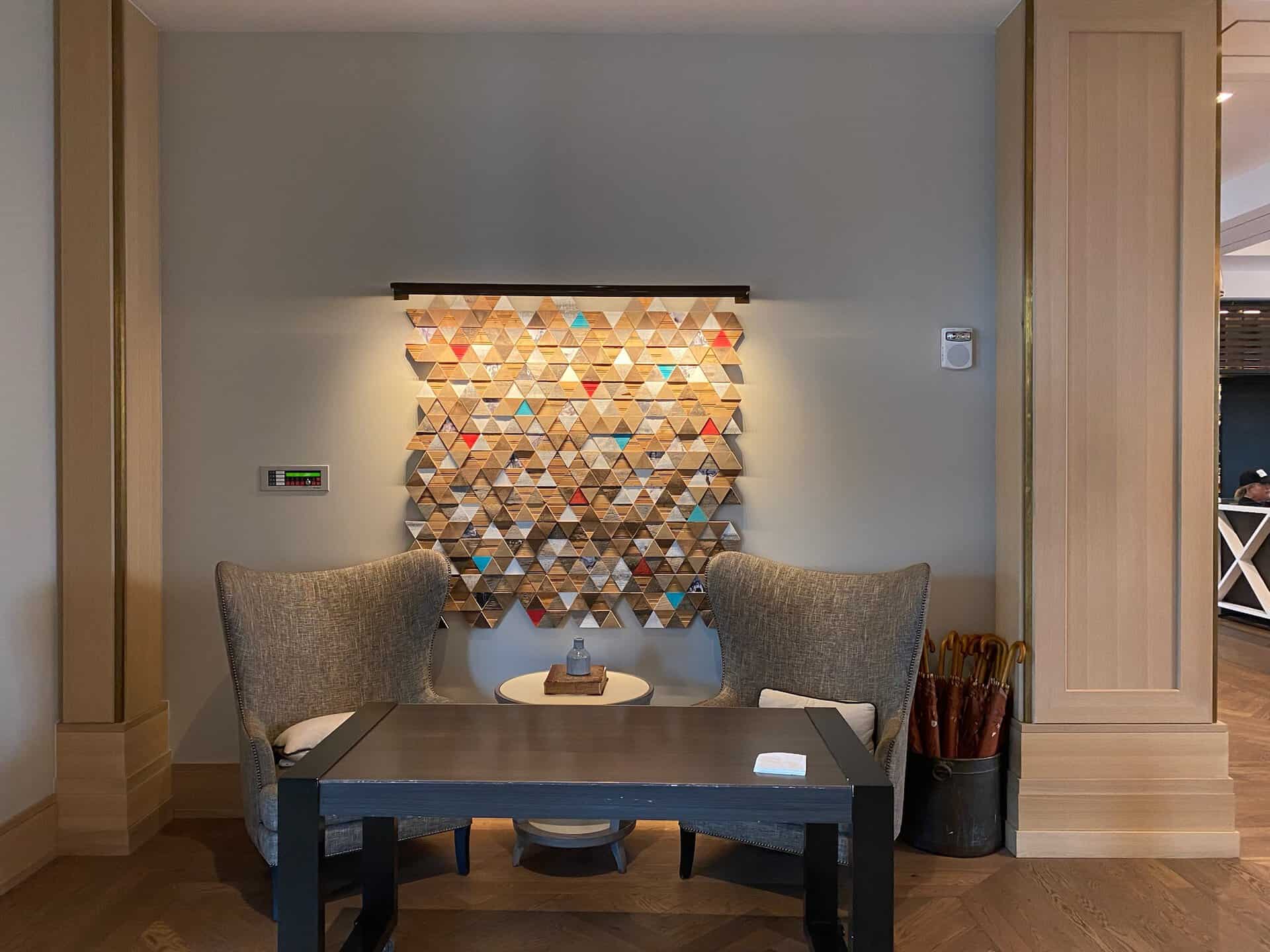Two armchairs and a small coffee table in front of a wall-mounted geometric art piece evoke the vibrant spirit of Nashville. An umbrella stand is thoughtfully placed on the right.