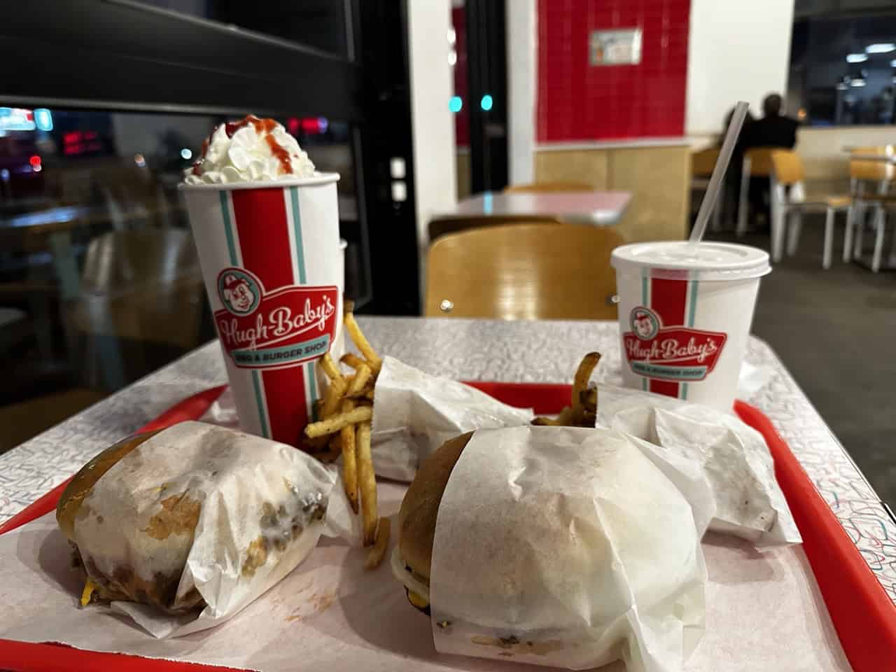 A Nashville-inspired fast-food meal on a tray, featuring two wrapped burgers, crispy fries, a creamy milkshake crowned with whipped cream, and a chilled drink cup.