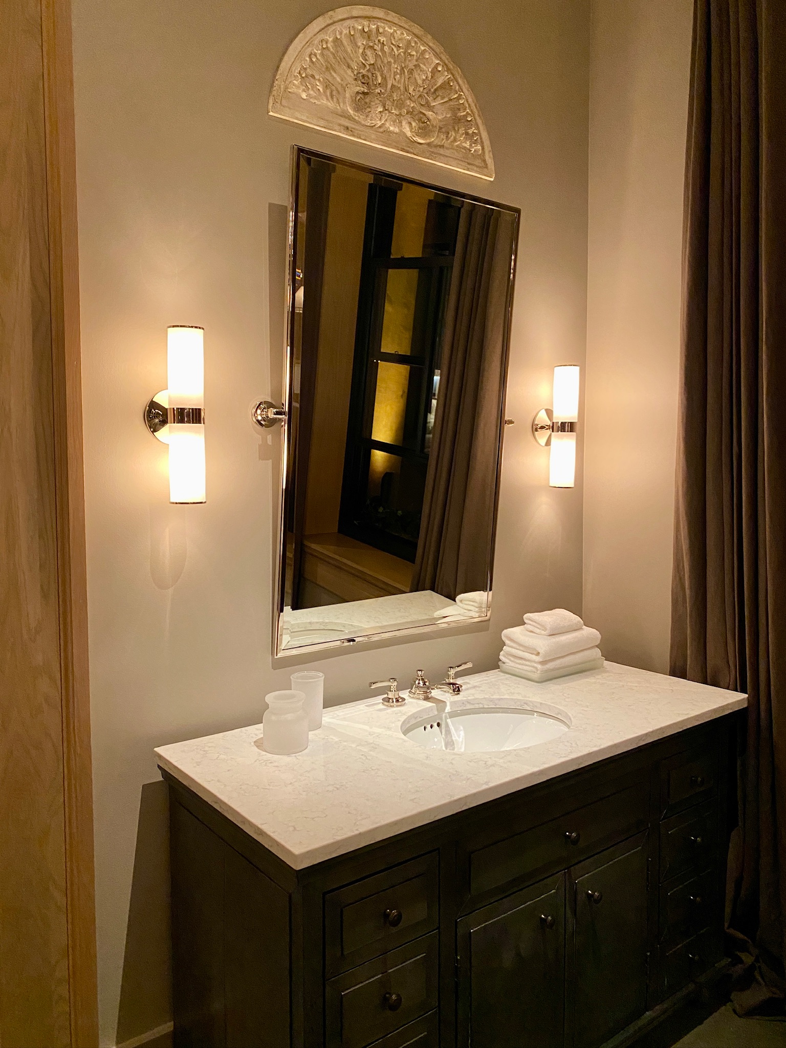 A Nashville-inspired bathroom vanity with a white countertop, sink, stacked towels, and two wall-mounted lights flanking a rectangular mirror.