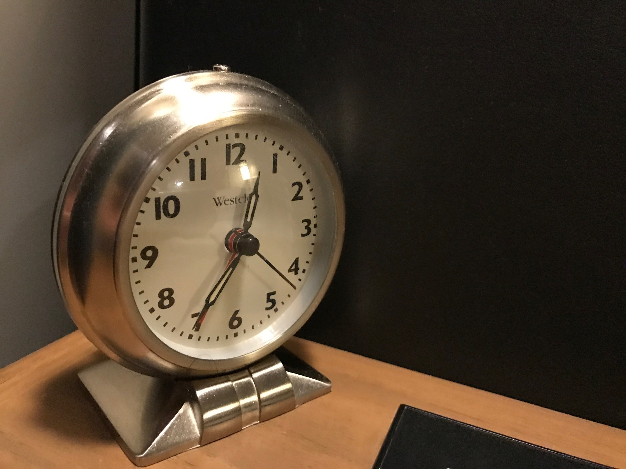 A silver analog Westclox alarm clock on a wooden surface shows the time as 6:42:21.
