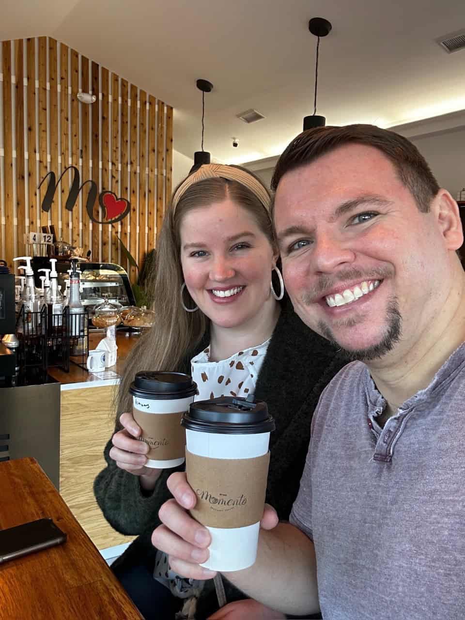 A man and a woman smile and hold coffee cups inside a Nashville café with charming wooden decor.