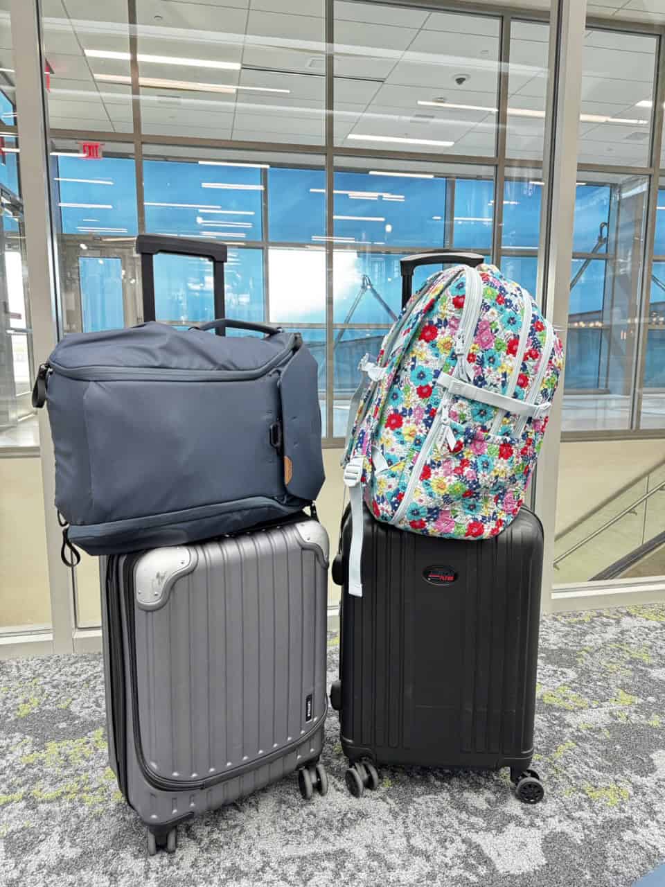 Two suitcases sit in the bustling Nashville airport terminal, with a black bag perched on the left one and a floral backpack on the right.