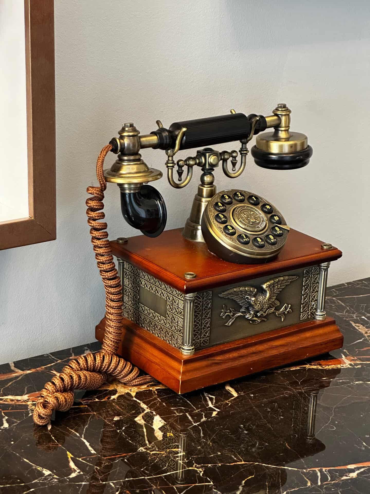 A vintage rotary telephone with a brass and wood design, adorned with an eagle emblem, sits elegantly on a marble tabletop—perfect for adding a touch of Nashville charm to your decor.