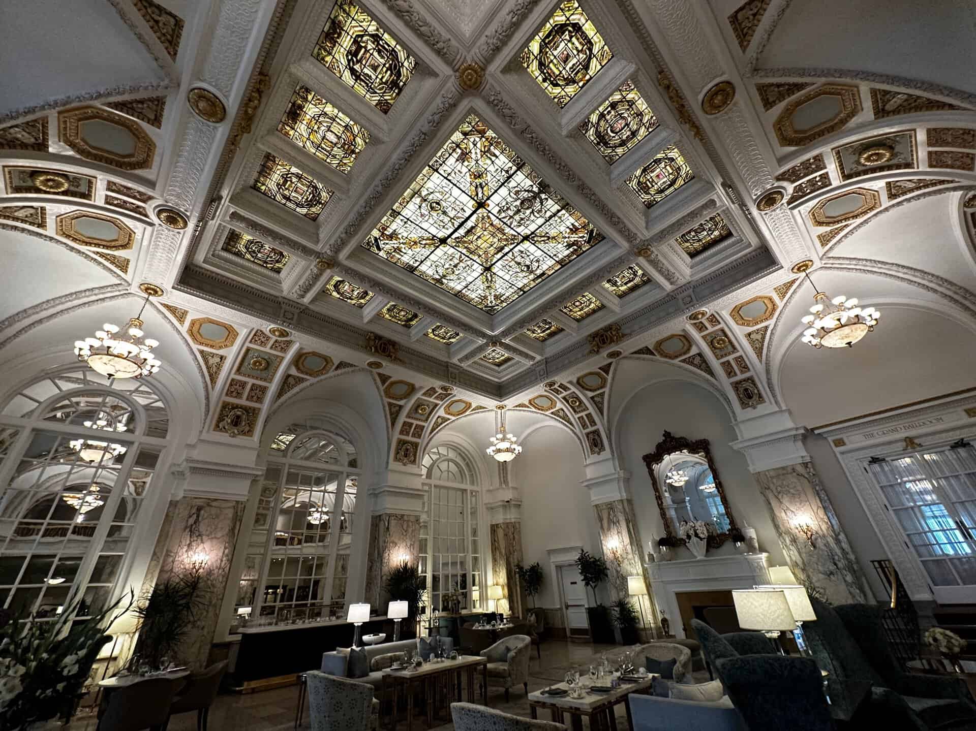 The elegant Nashville hotel lobby features an ornate stained glass ceiling, chandeliers, and classical architectural details. Plush seating alongside decorative plants enhances the sophisticated ambiance, making it a luxurious retreat in the heart of Music City.