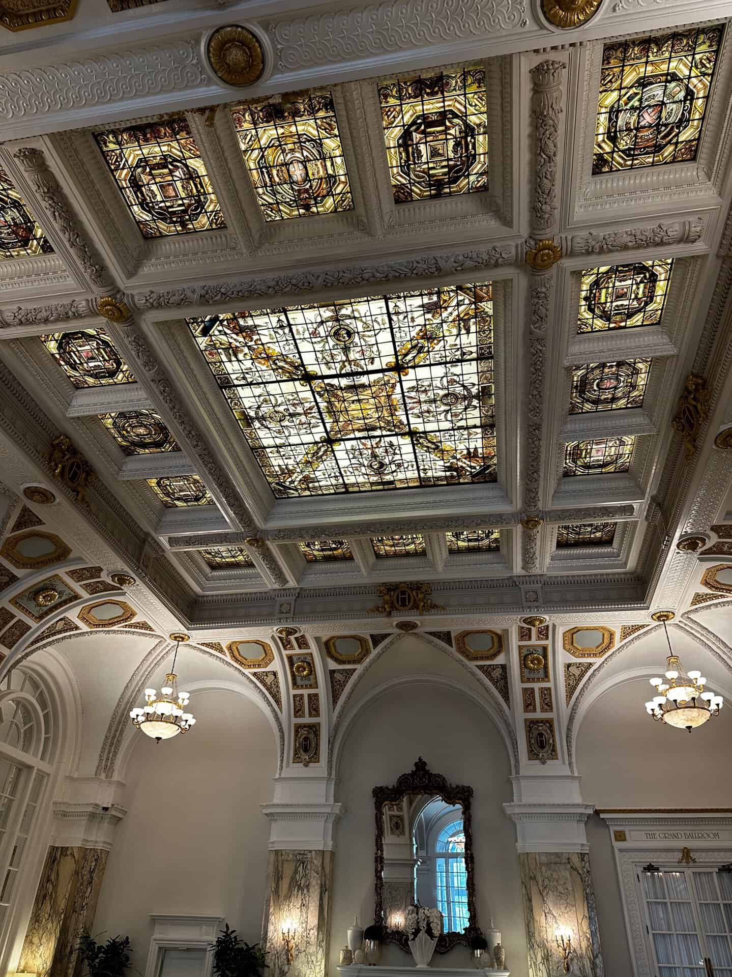 An elegant room in Nashville features an ornate ceiling with stained glass panels and decorative moldings, flanked by arched windows and chandeliers.