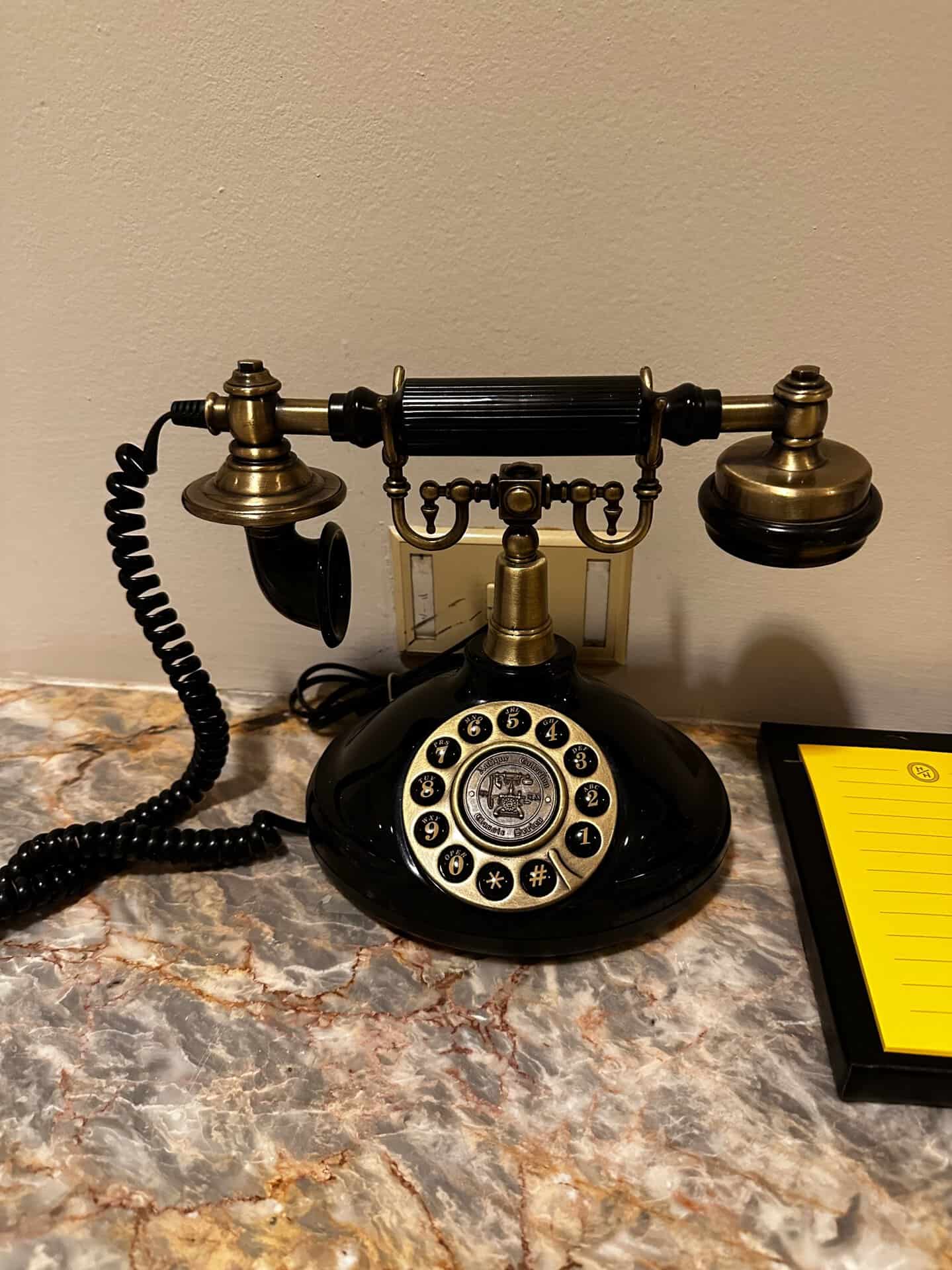A vintage rotary phone with a brass receiver and dial sits charmingly on a marble surface, resembling an artifact from old Nashville, accompanied by a yellow notepad.