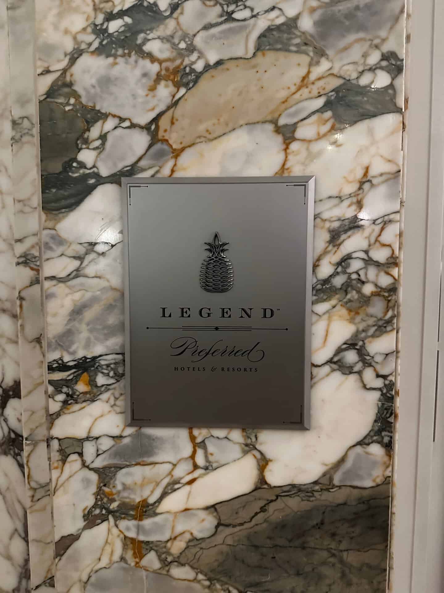 A silver plaque featuring a pineapple design and the text "LEGEND Preferred Hotels & Resorts" is elegantly mounted on a marble wall with gray, white, and gold veining. This exquisite piece captures the essence of luxury reminiscent of Nashville's renowned hospitality.