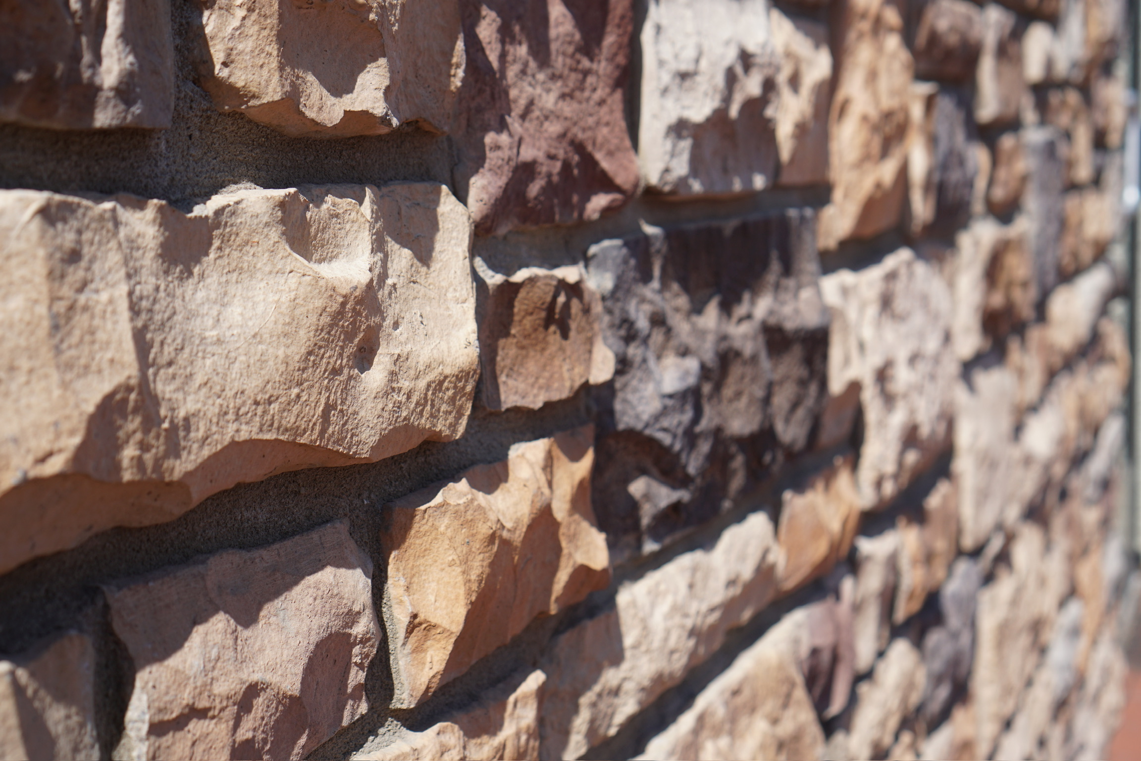 Close-up view of a textured stone wall with irregularly shaped, multi-colored stones stacked and cemented together.