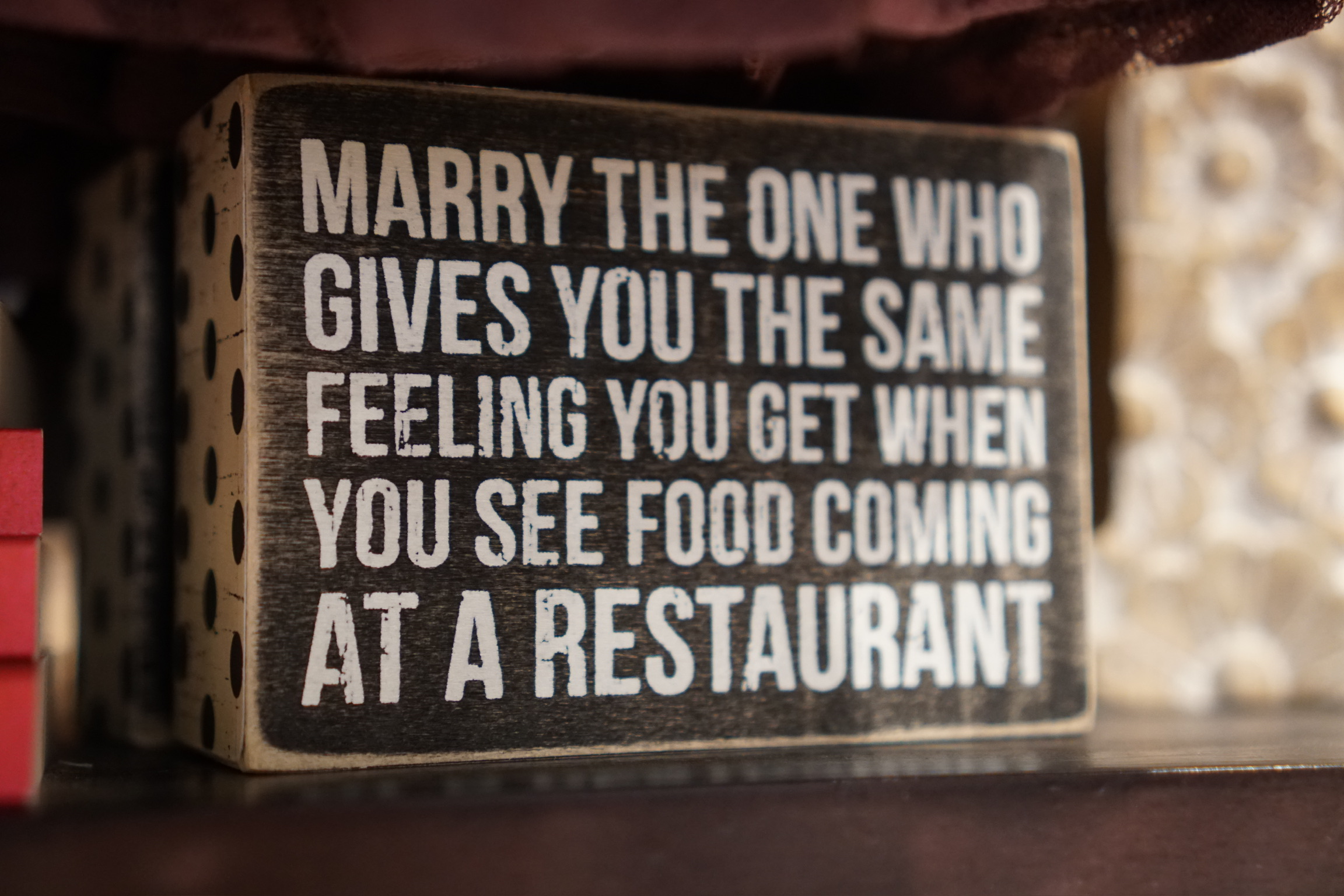 A wooden block with text reads: "Marry the one who gives you the same feeling you get when you see food coming at a restaurant.