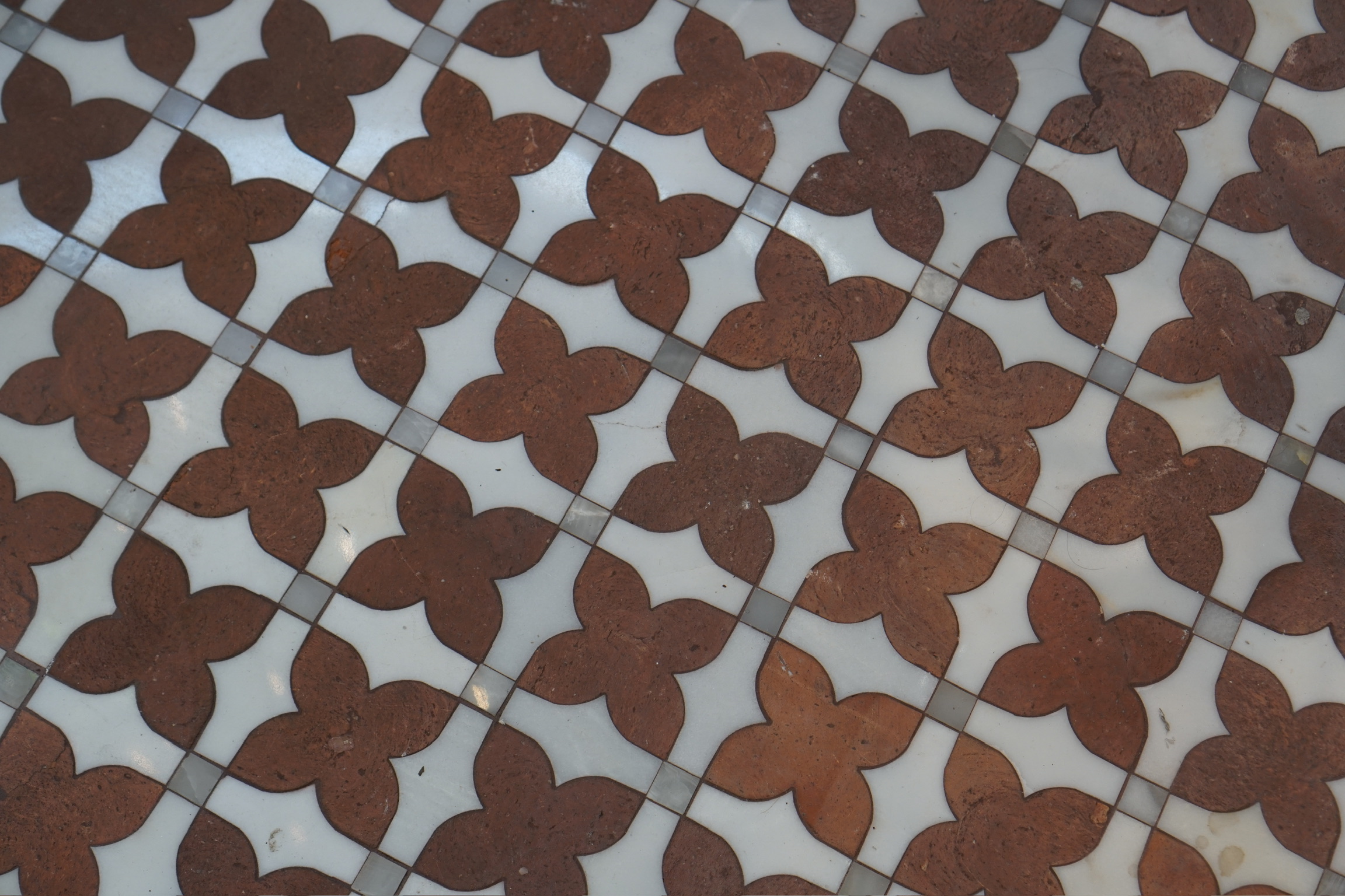 A close-up view of a tiled surface featuring a repeating pattern of brown four-petal shapes on a white background.
