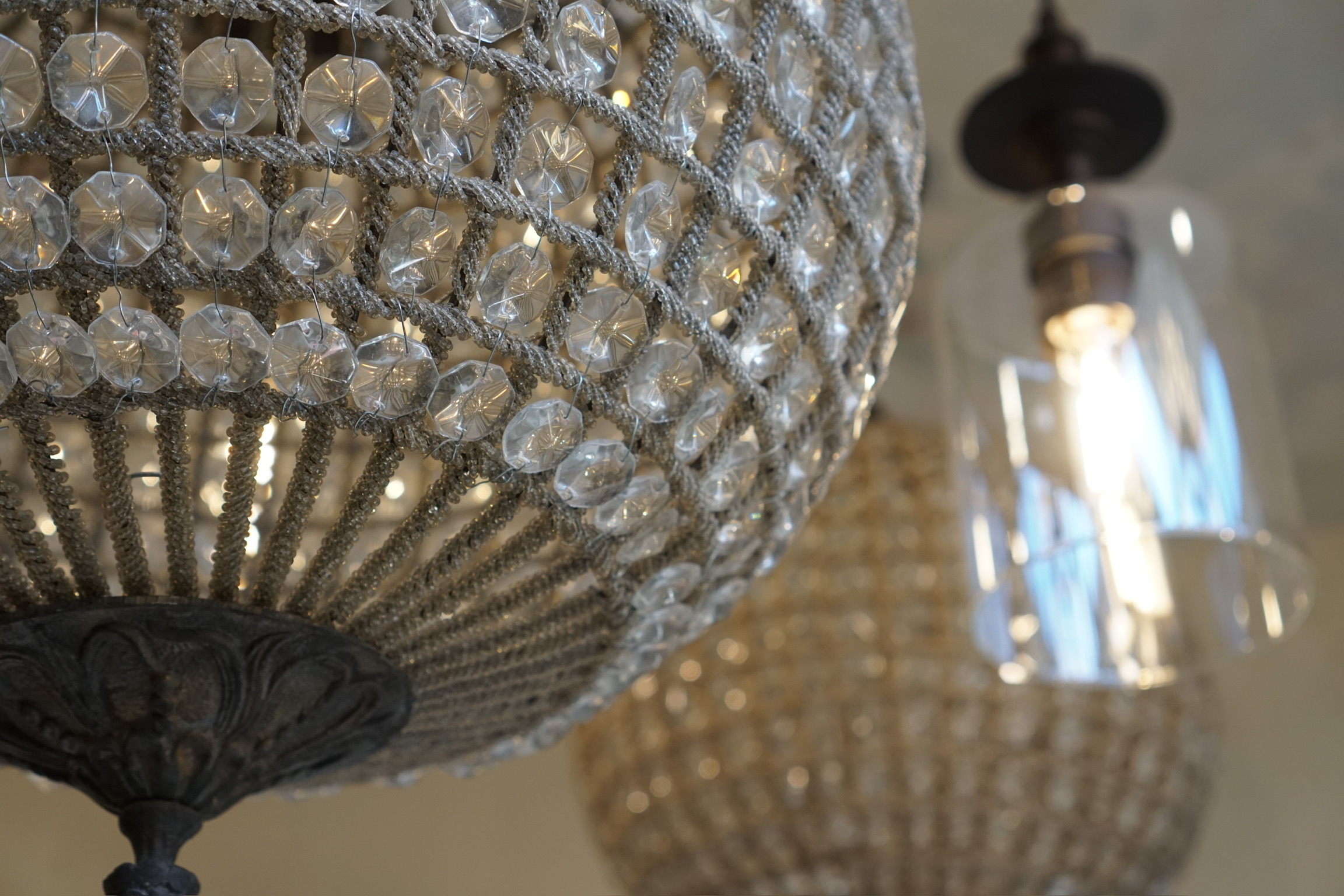 Close-up of a decorative chandelier with crystal beads in the foreground and a modern glass pendant light in the background.